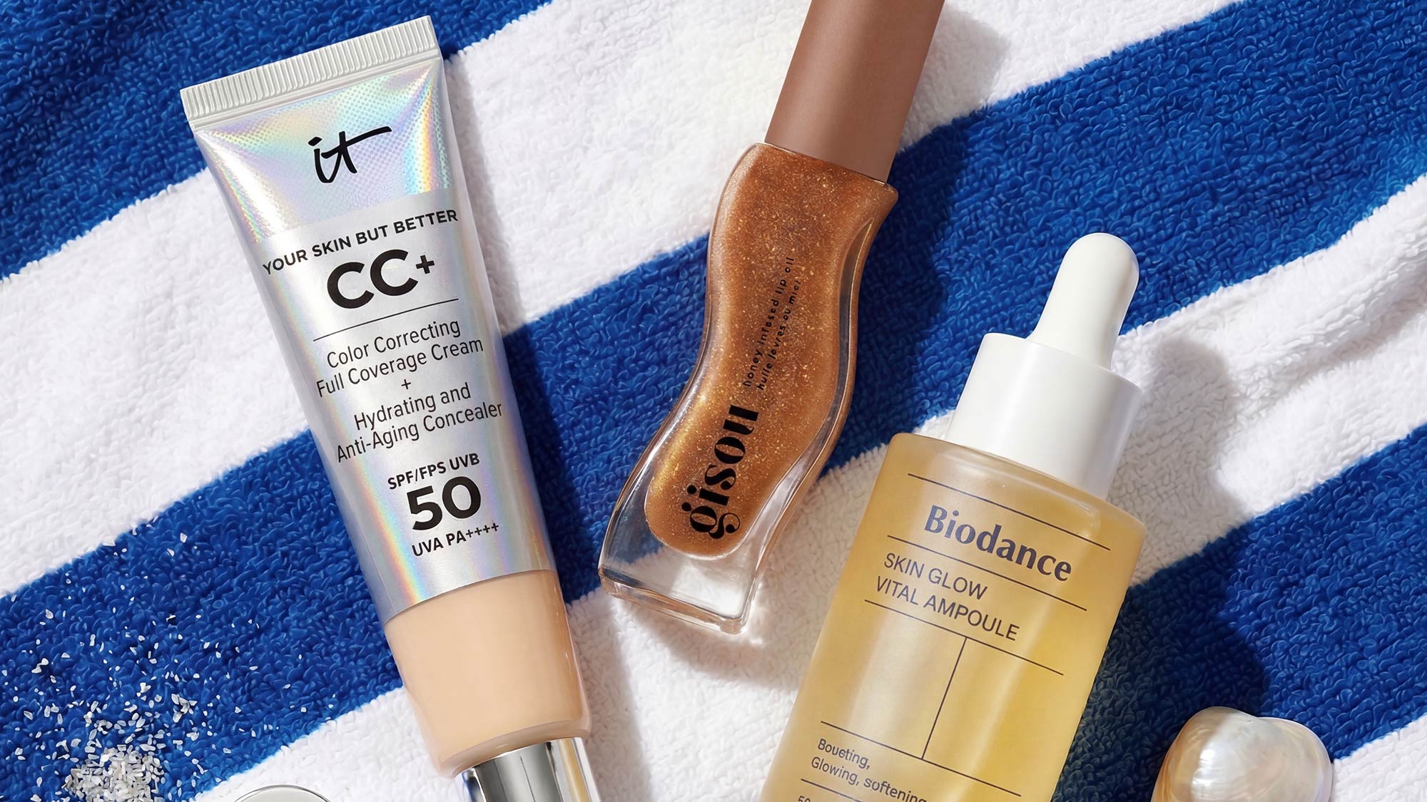 Selection of summer beauty products including CC cream, nail polish, and facial serum displayed on striped blue and white towel