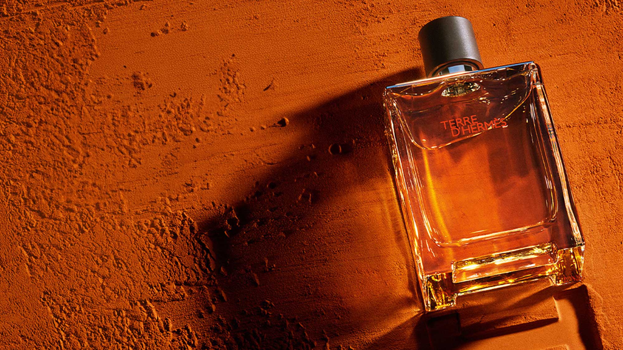 Terre d'Hermès fragrance bottle with amber liquid on textured orange background, complementary 5ml EDT offer