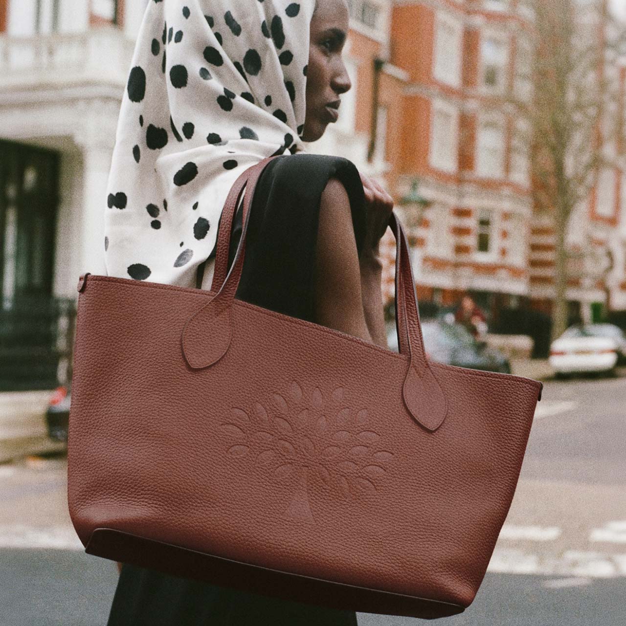 Woman wearing polka dot outfit carrying burgundy leather Mulberry tote bag on city street