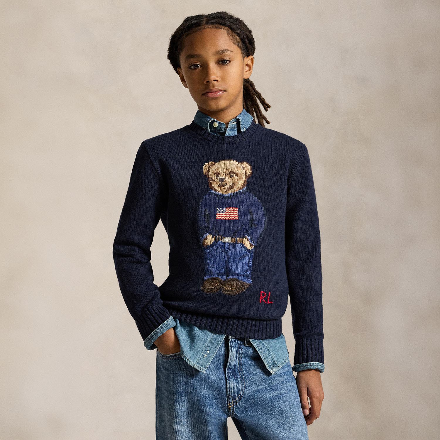 Young boy wearing navy knit jumper with teddy bear design and denim shirt layered underneath