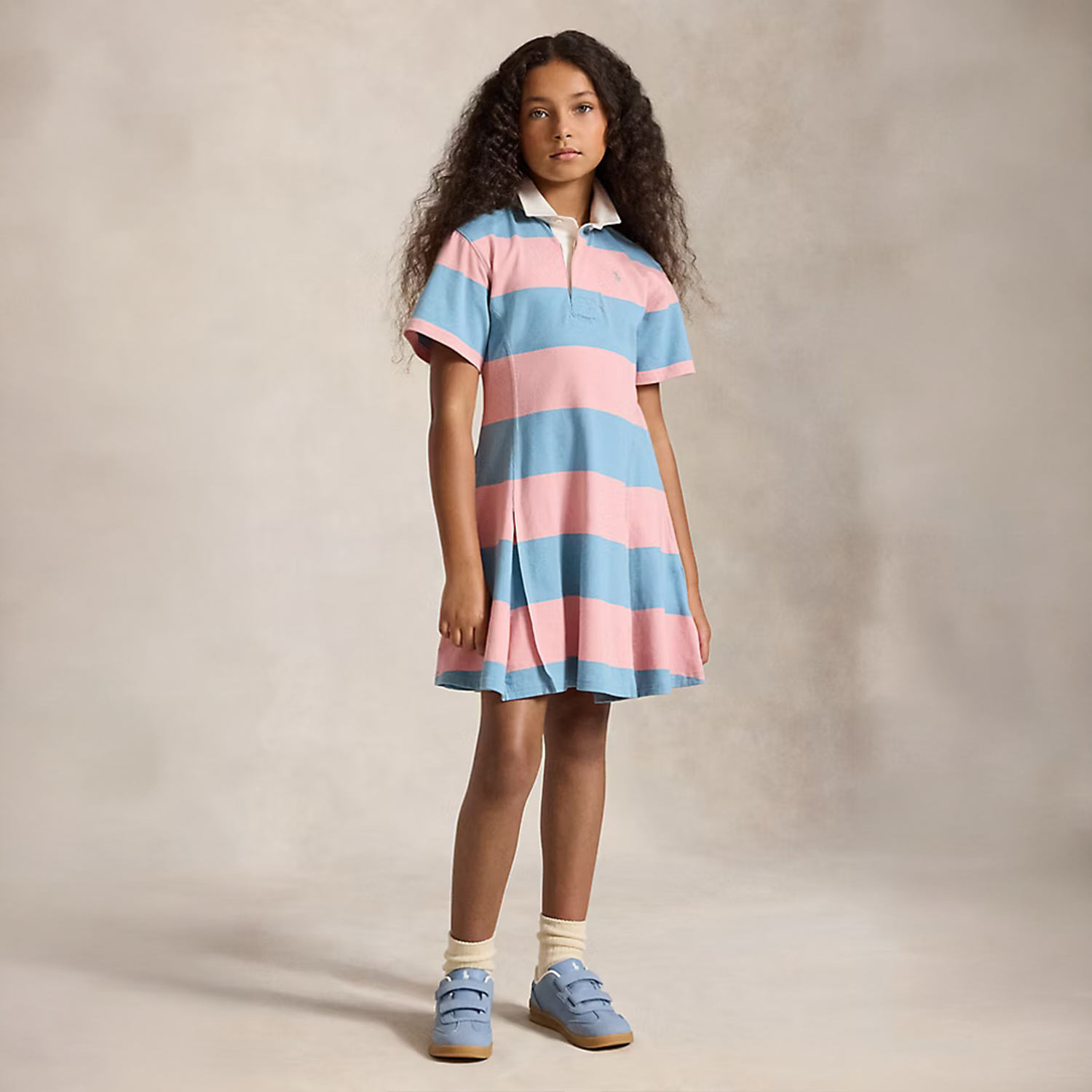 Young girl wearing blue and pink striped rugby shirt dress with collar and blue sandals