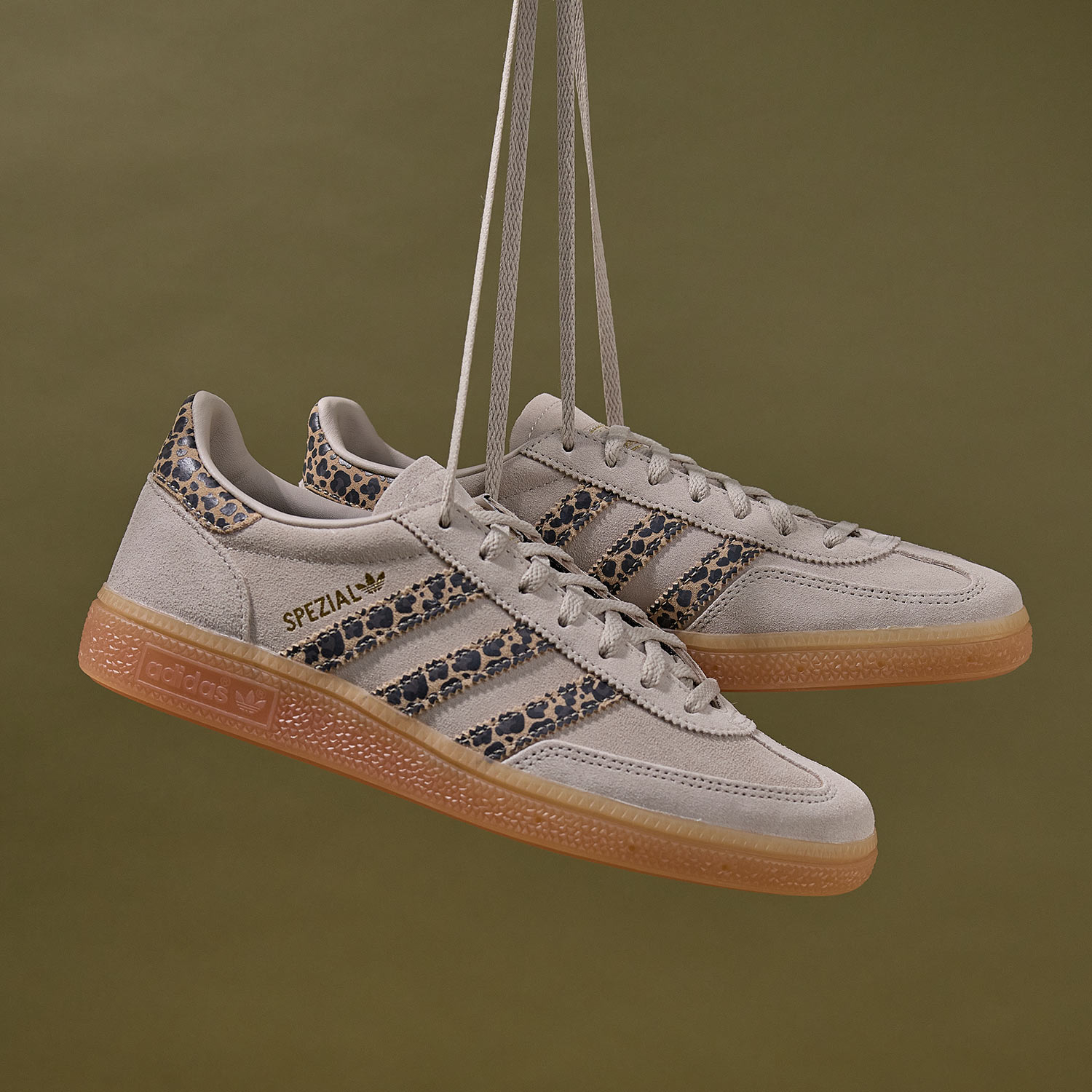 Pair of Adidas Spezial trainers in cream with leopard print stripes and gum sole, suspended on rope