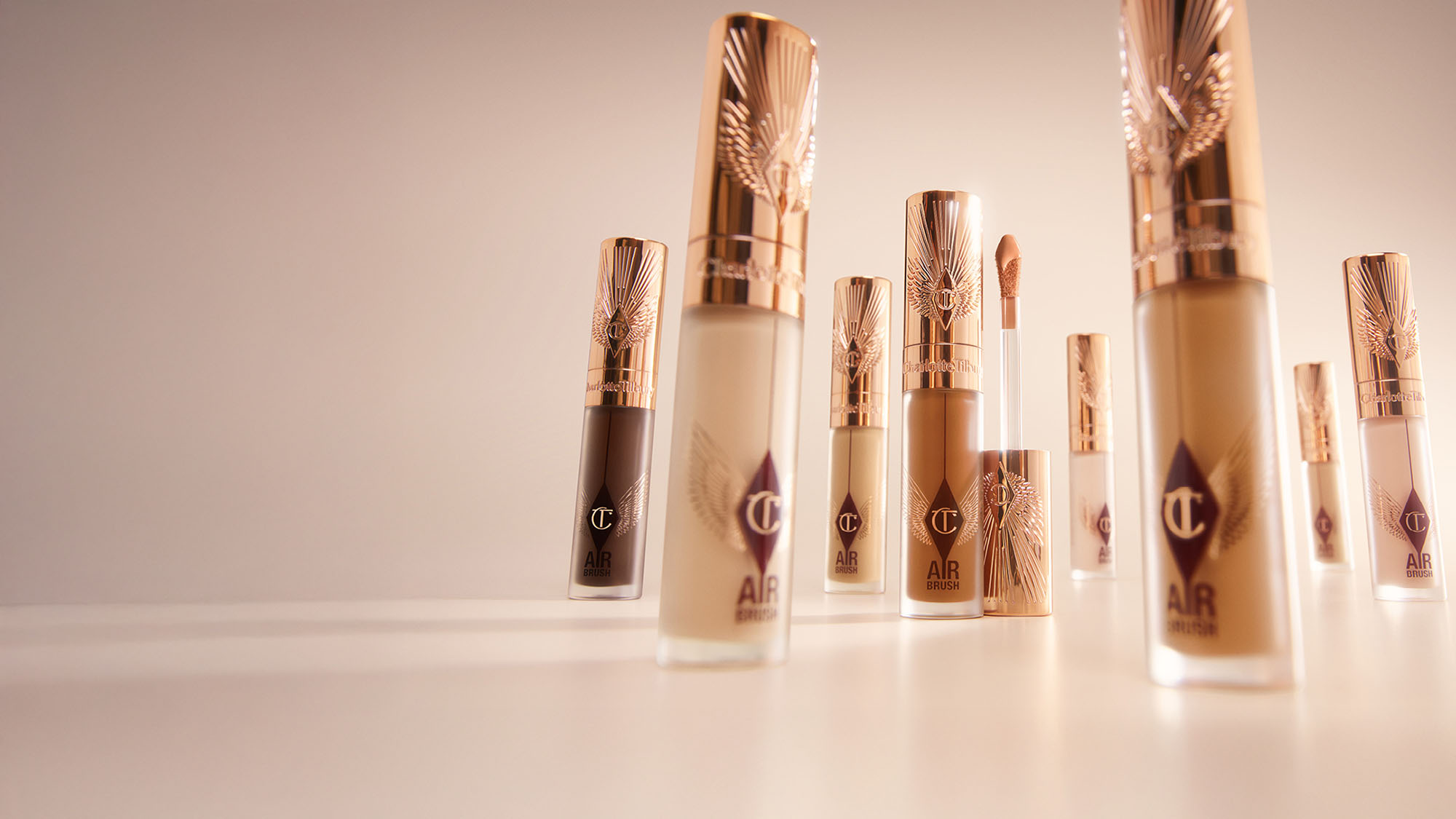 Various shades of makeup concealers in elegant tubes with rose gold caps, arranged on a light surface.