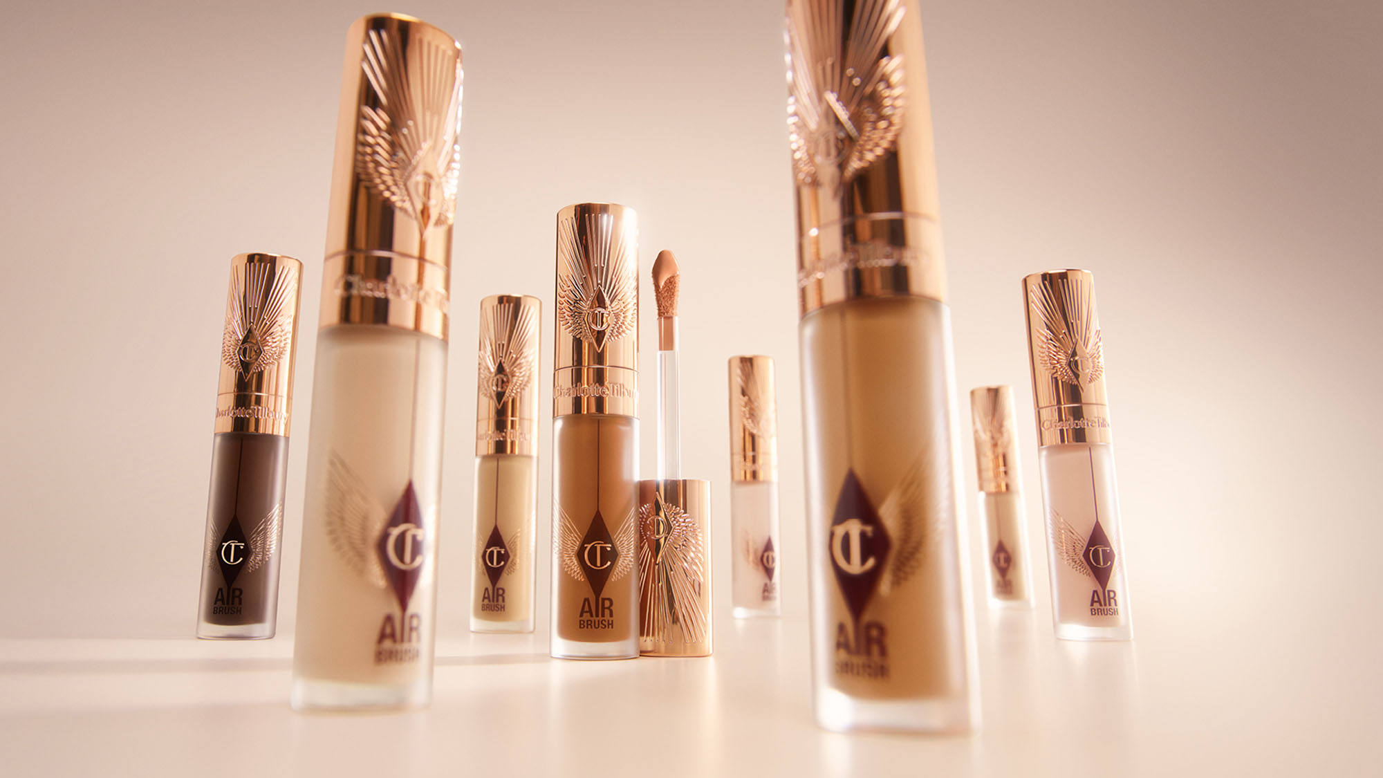 Various shades of makeup concealers in elegant tubes with rose gold caps, arranged on a light surface.