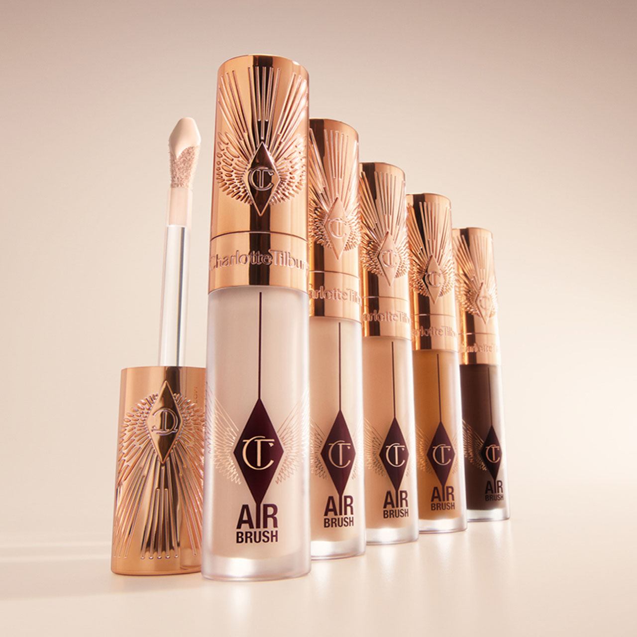 A set of six Charlotte Tilbury Airbrush makeup products in a gradient of shades, with rose gold caps and applicators.