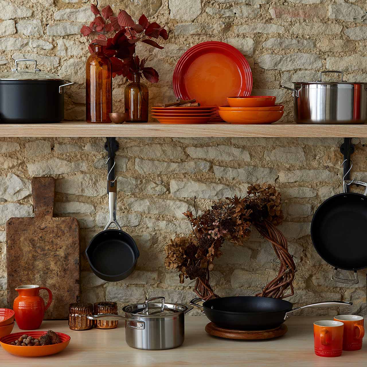 Kitchen shelf with colorful dishes, pots, pans, and autumn-themed decor against a stone wall.