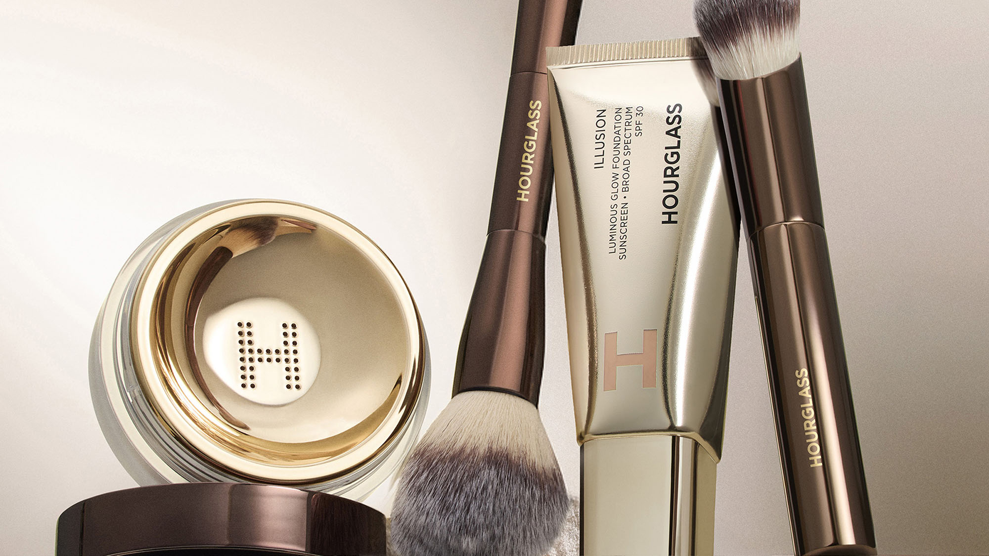 Makeup brushes, a tube, and a container with the Hourglass logo on a shelf.