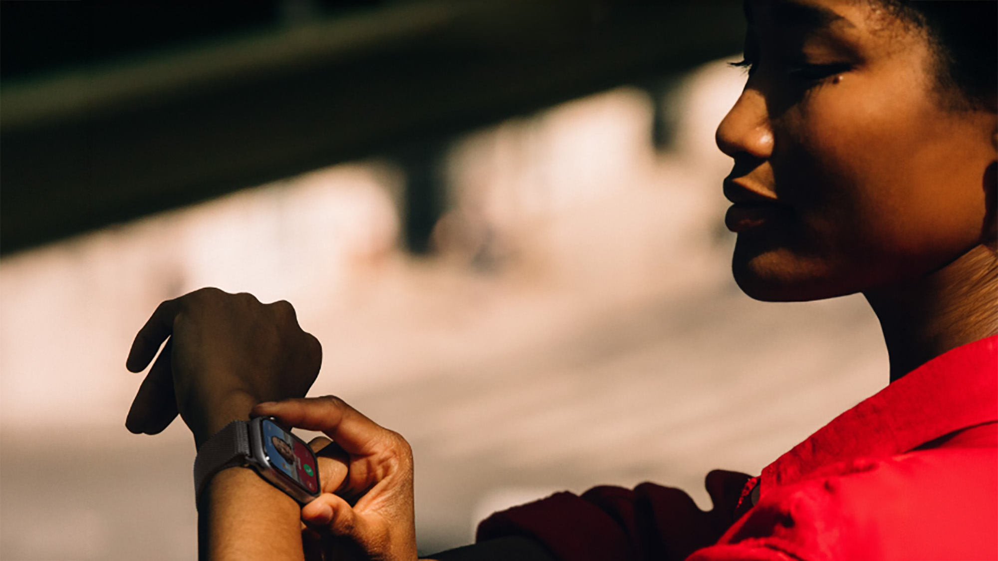 Person in red jacket wearing smartwatch outdoors with sunny background