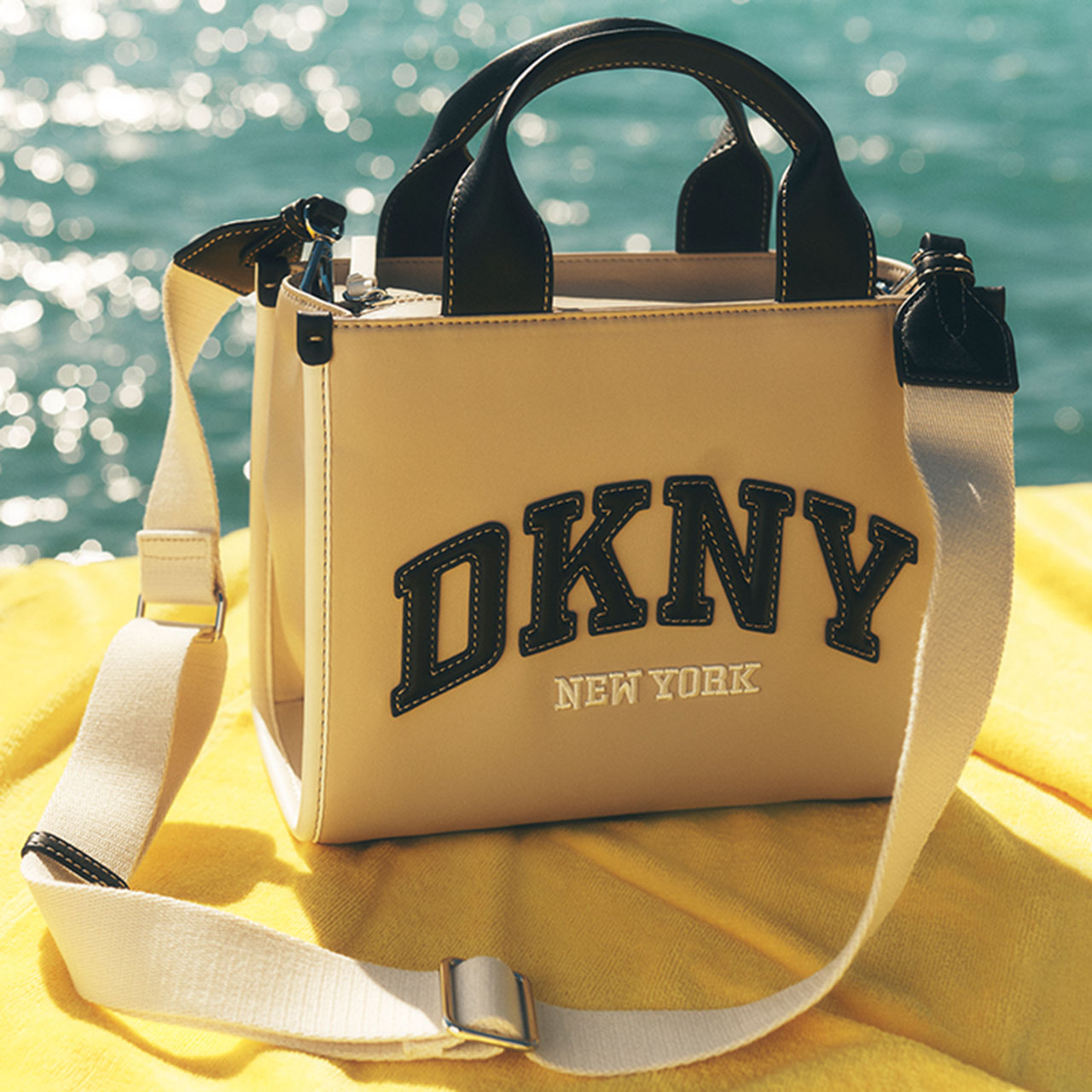 Cream and black tote bag on yellow towel by sparkling turquoise sea