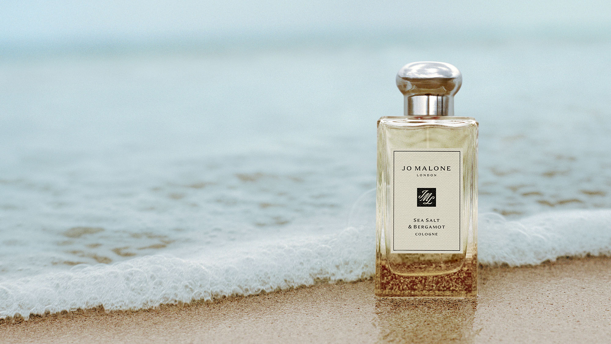 Jo Malone Sea Salt & Bergamot cologne bottle on sandy beach with ocean waves in background