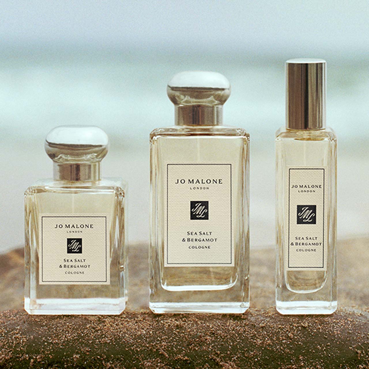 Three glass fragrance bottles with sea salt and bergamot cologne on sandy beach