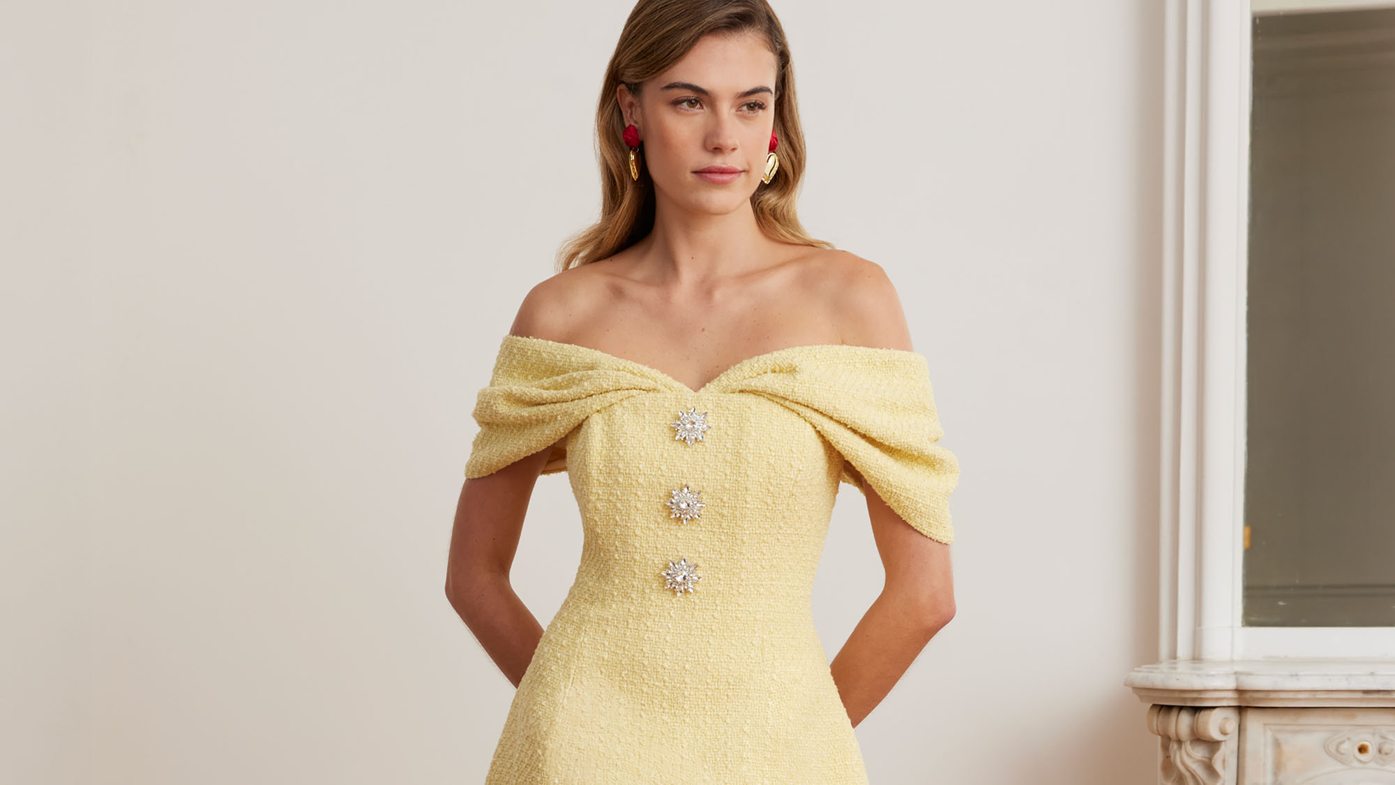 Woman wearing pale yellow off-shoulder dress with crystal embellishments and red drop earrings