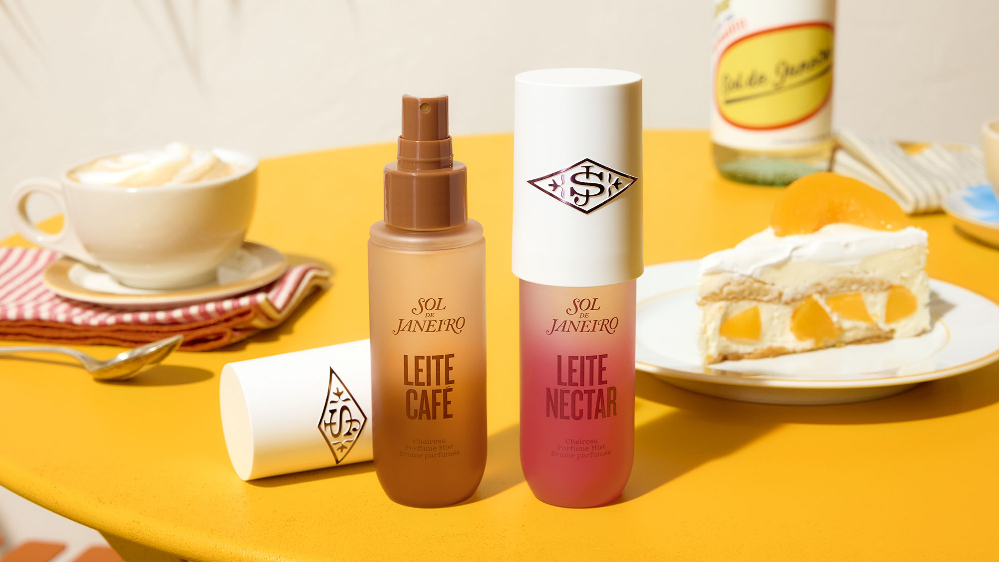 Sol de Janeiro Leite Café and Leite Nectar perfume mists displayed on yellow surface with coffee cup and cake