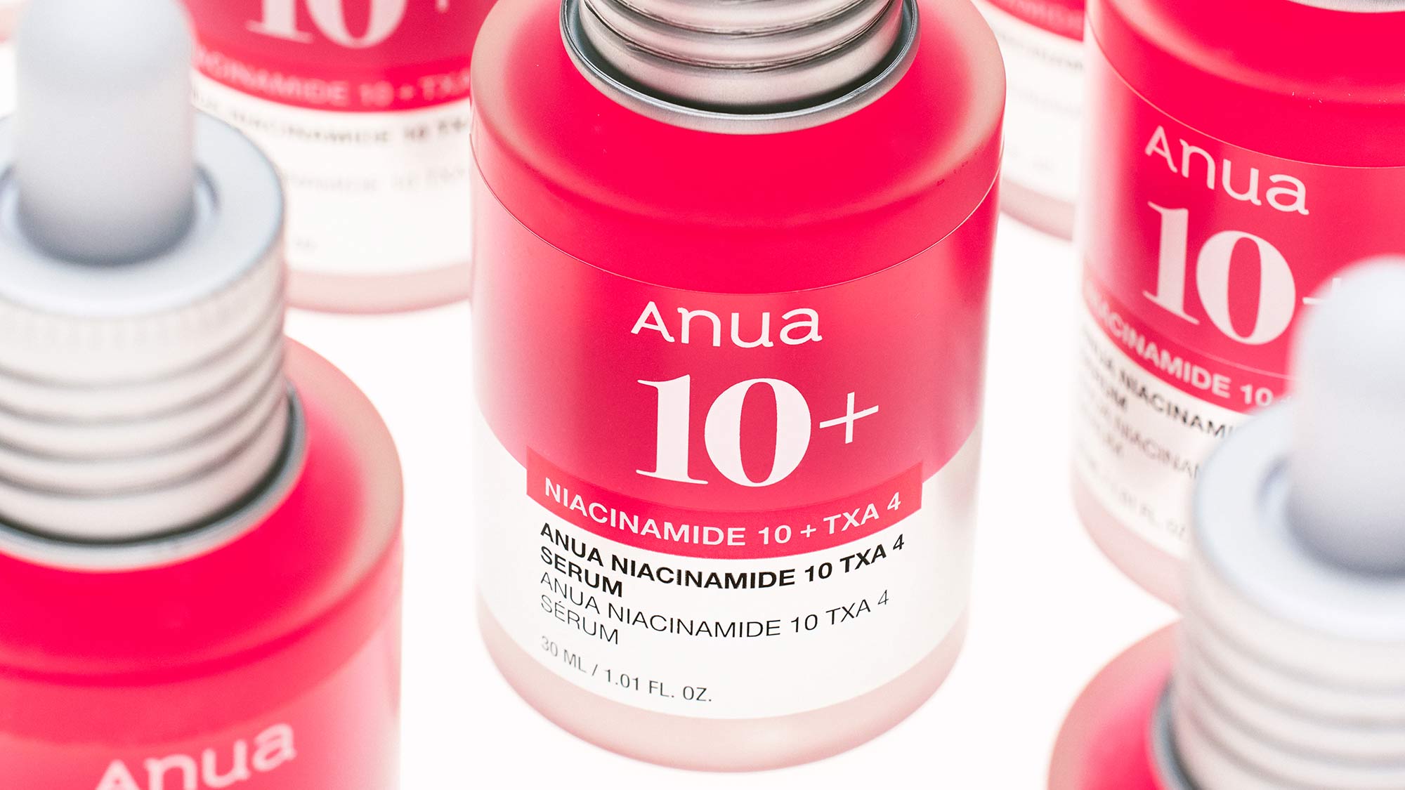 ANUA Niacinamide 10+ TXA 4 serum bottles with bright pink caps and white base on white surface