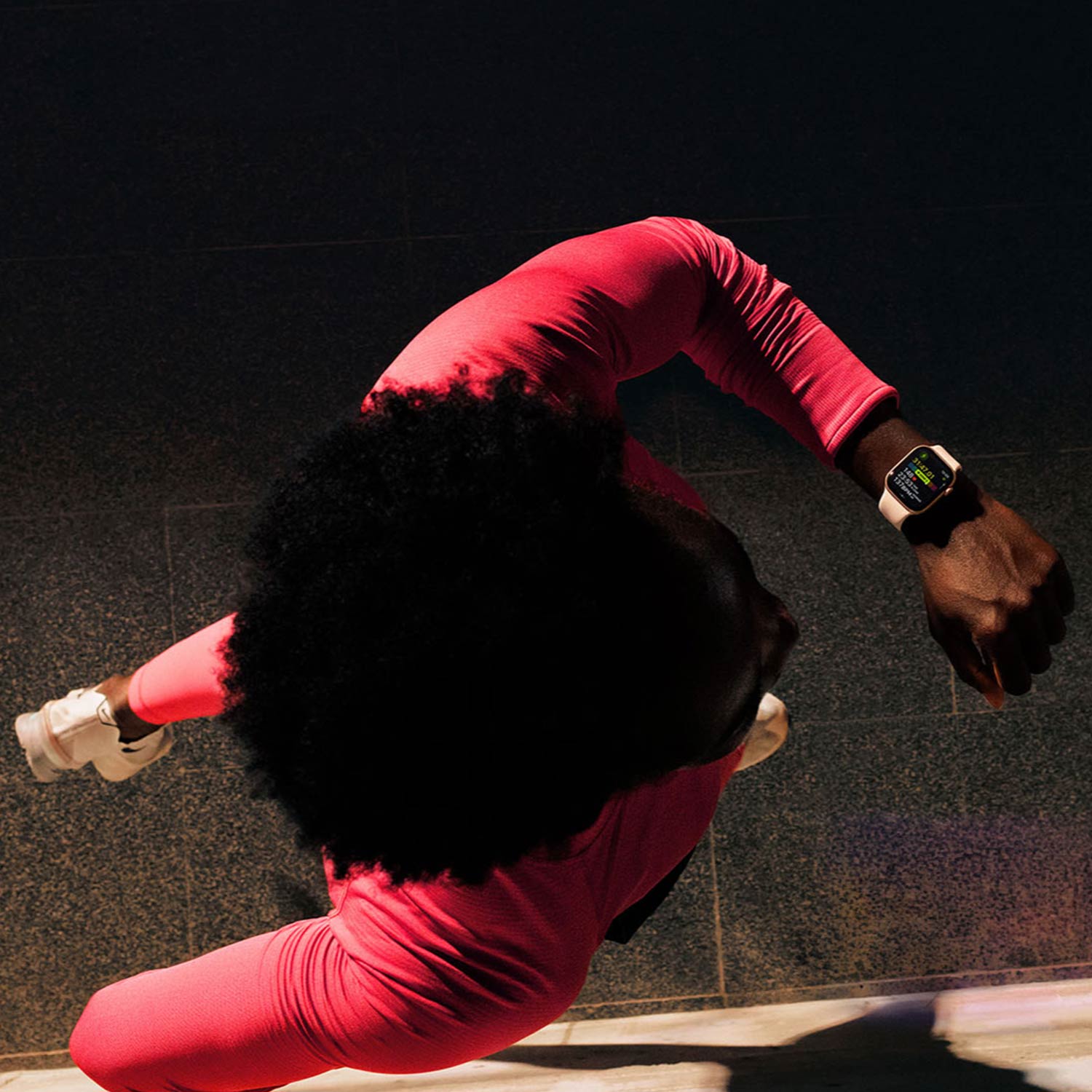Person wearing bright pink athletic wear and smartwatch doing a push-up position on dark floor