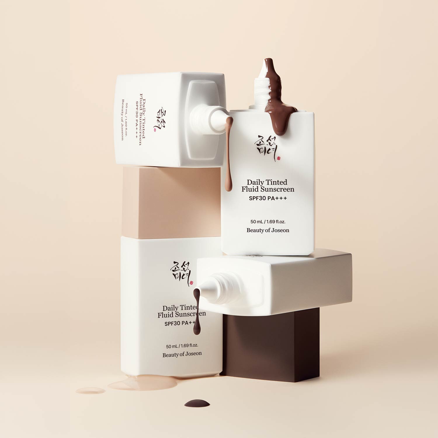 Beauty of Joseon Daily Tinted Fluid Sunscreen bottles displayed on cream and brown blocks, showing product texture swatches
