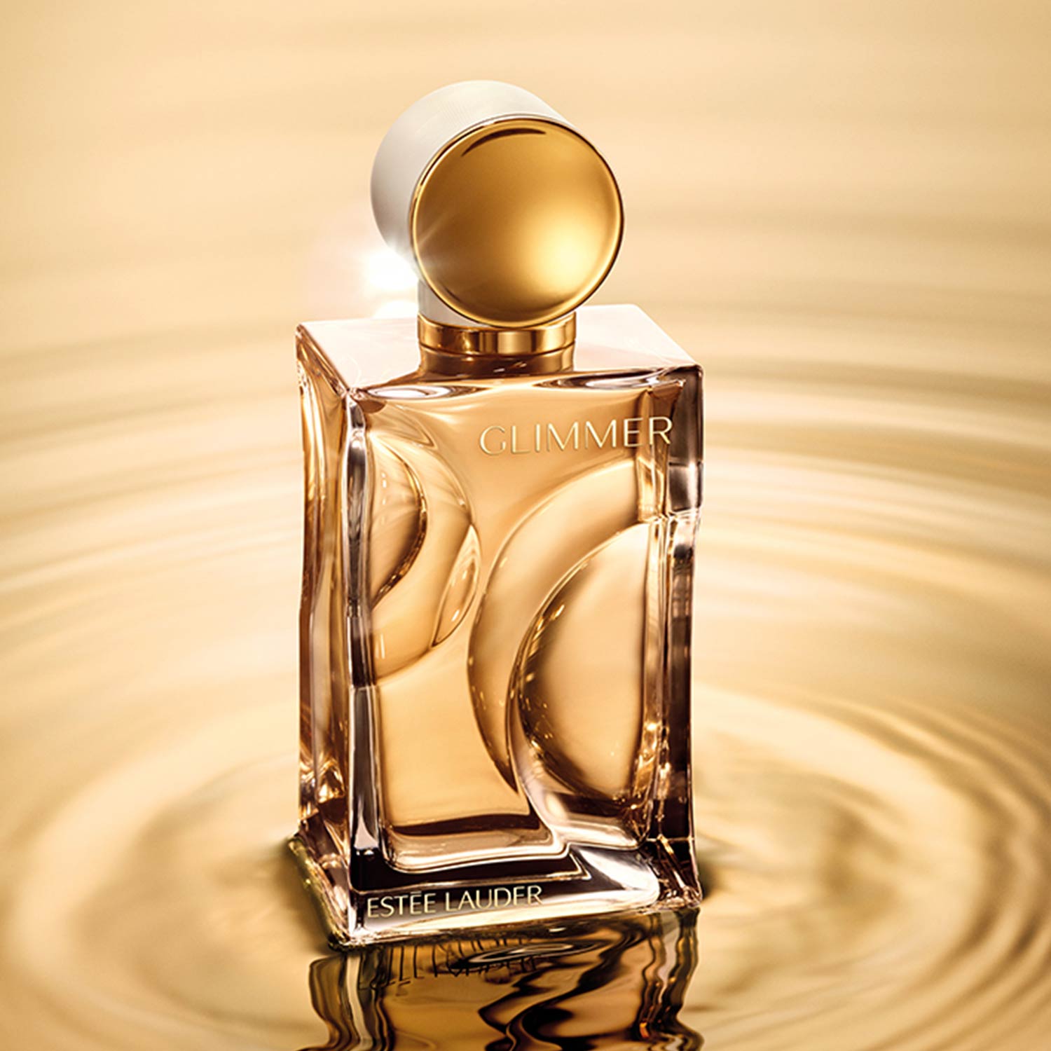 Est&eacute;e Lauder Glimmer fragrance bottle with golden liquid and white cap against warm golden background