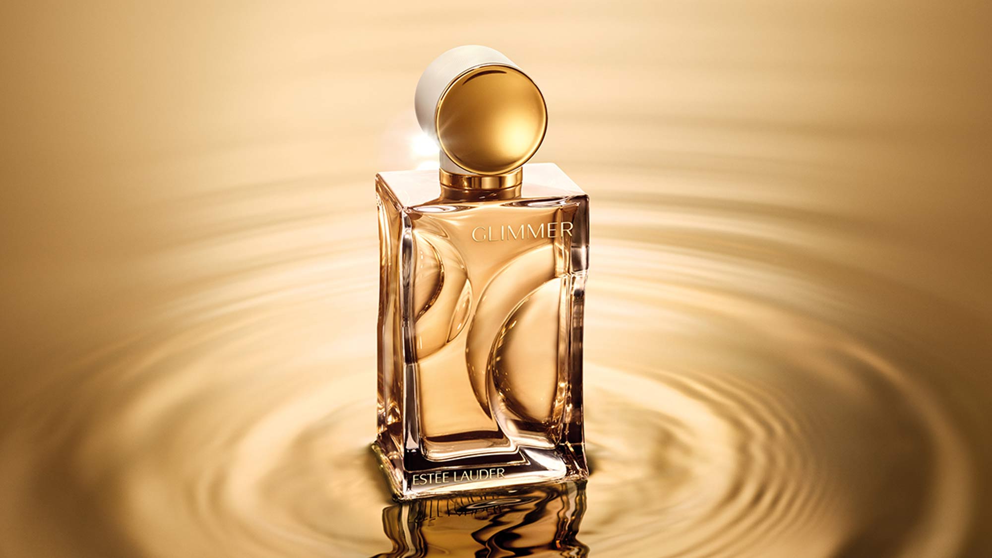 Estée Lauder Glimmer fragrance bottle with golden liquid and white cap against warm golden background