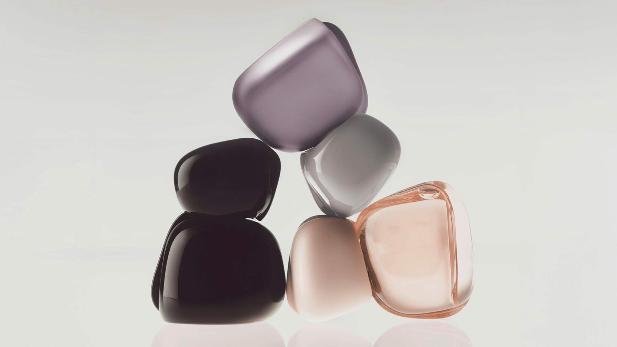 Four translucent fragrance bottles in purple, black, beige, and rose tones arranged on a neutral background