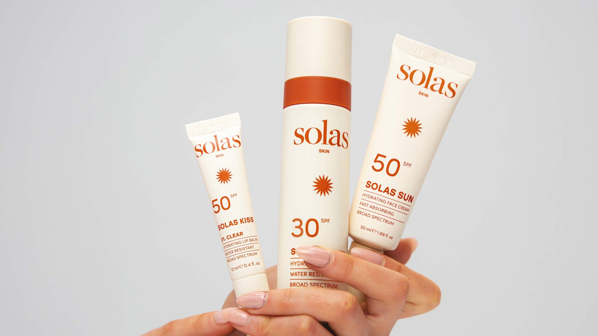 Three Solas Skin sunscreen products with SPF 50 and SPF 30 held in hand against neutral background
