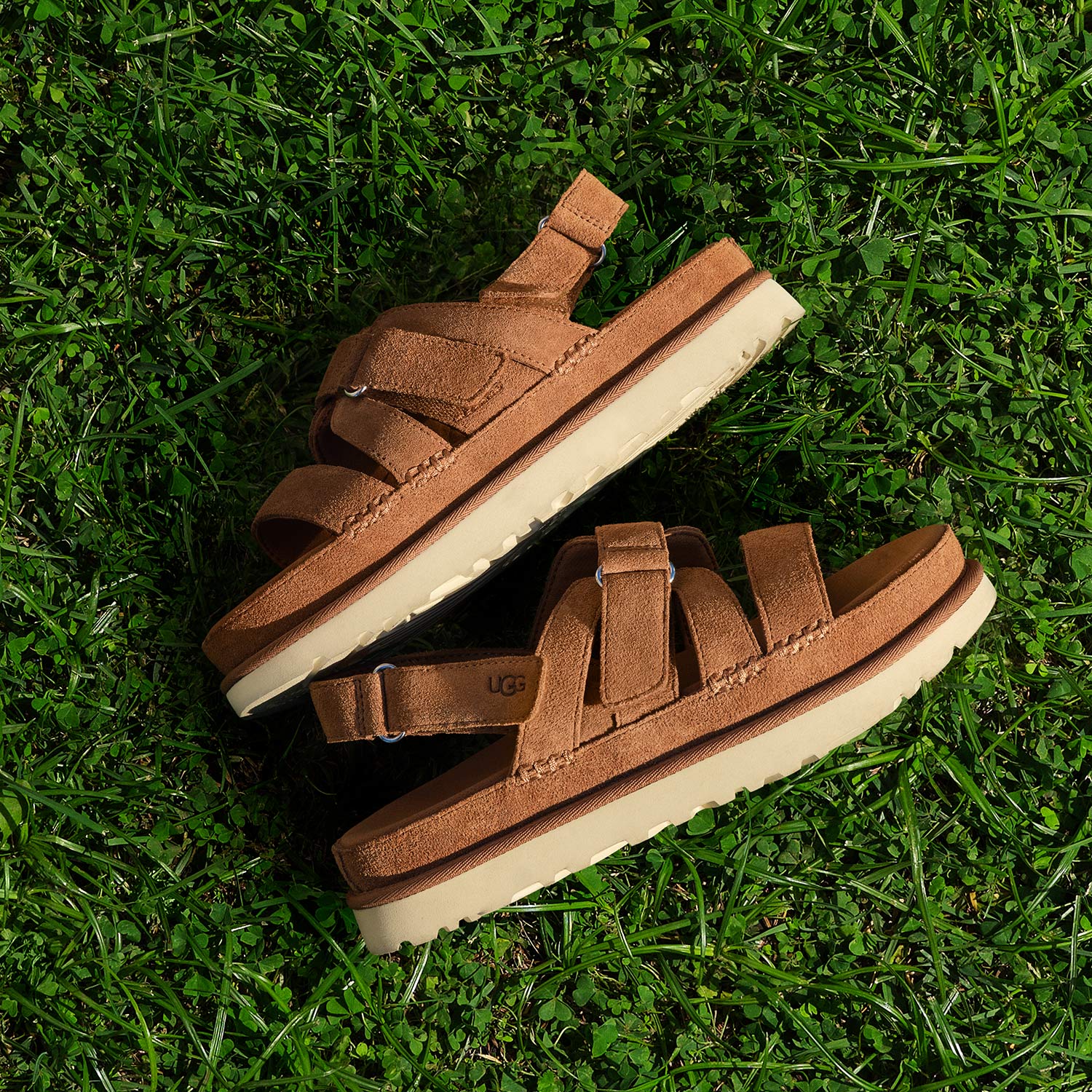 Pair of tan suede UGG sandals with cream soles displayed on vibrant green grass