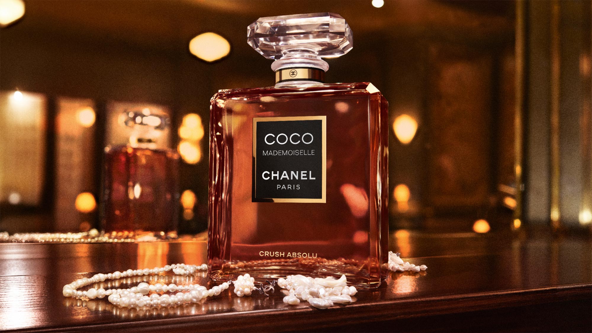 Chanel Coco Mademoiselle Crush Absolu fragrance bottle displayed with pearl necklaces in warm ambient lighting