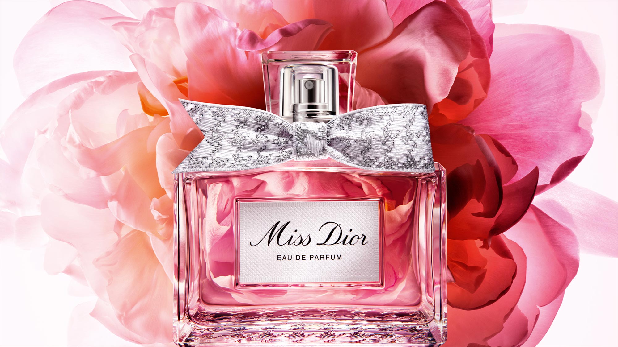 Miss Dior Eau De Parfum bottle with crystal bow stopper surrounded by pink peonies and rose petals
