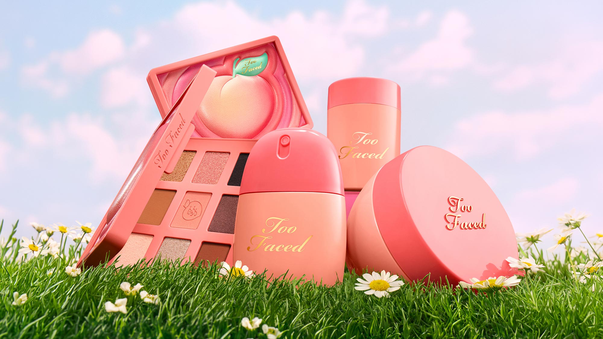 Too Faced Peach collection including eyeshadow palette, powder jars and lip products in coral and pink tones on grass with daisies