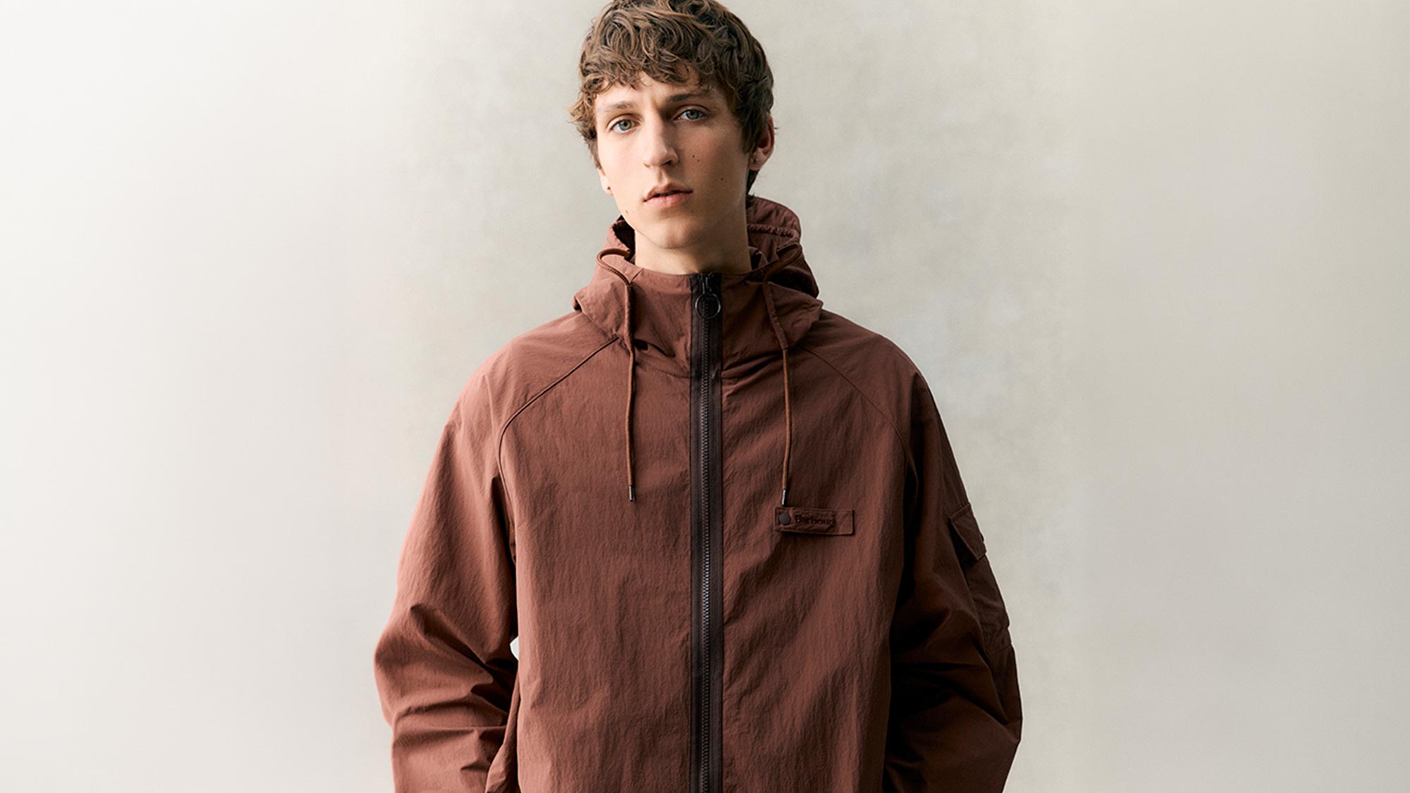 Young man wearing a terracotta brown hooded jacket with zip fastening