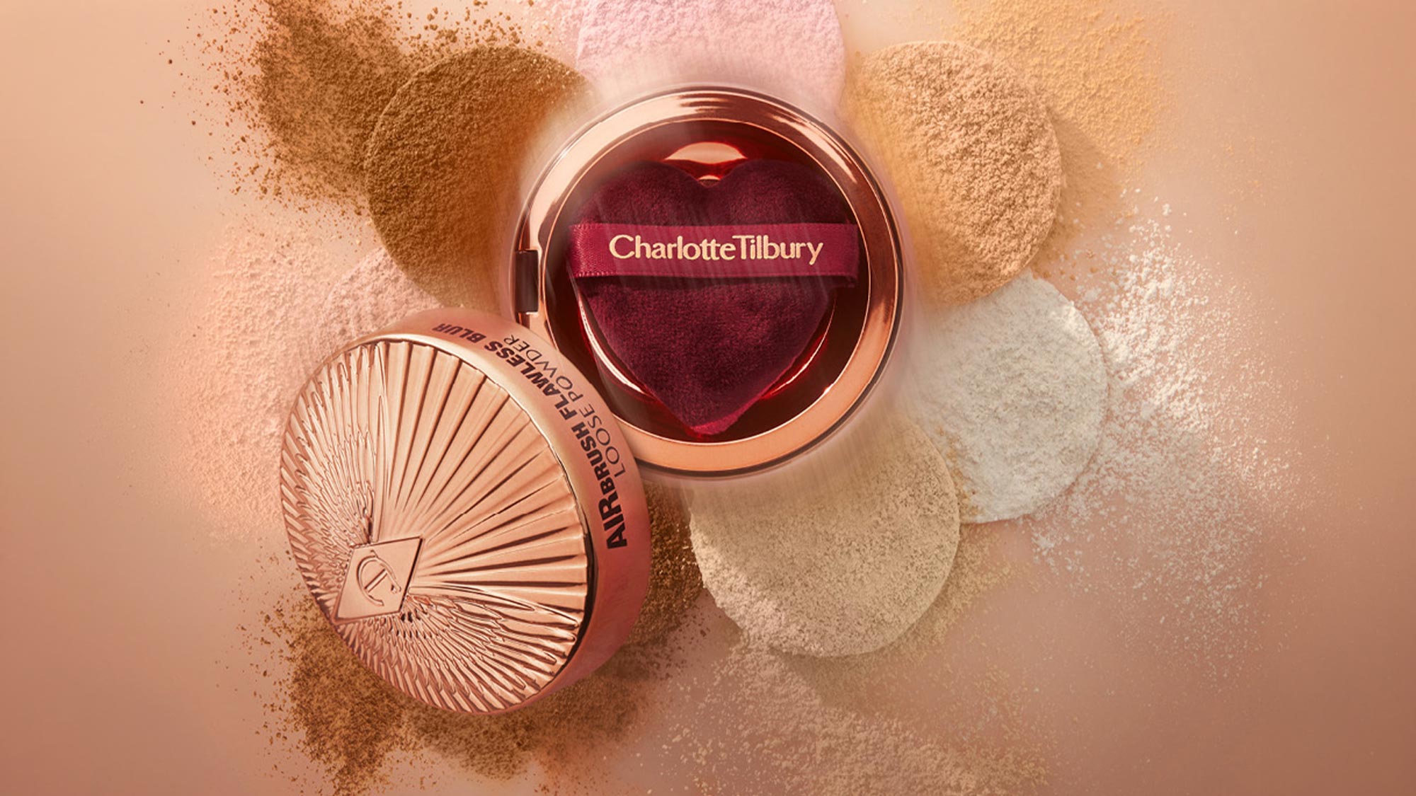 Charlotte Tilbury powder compact with rose gold case and fan-shaped brush surrounded by loose shimmer powders