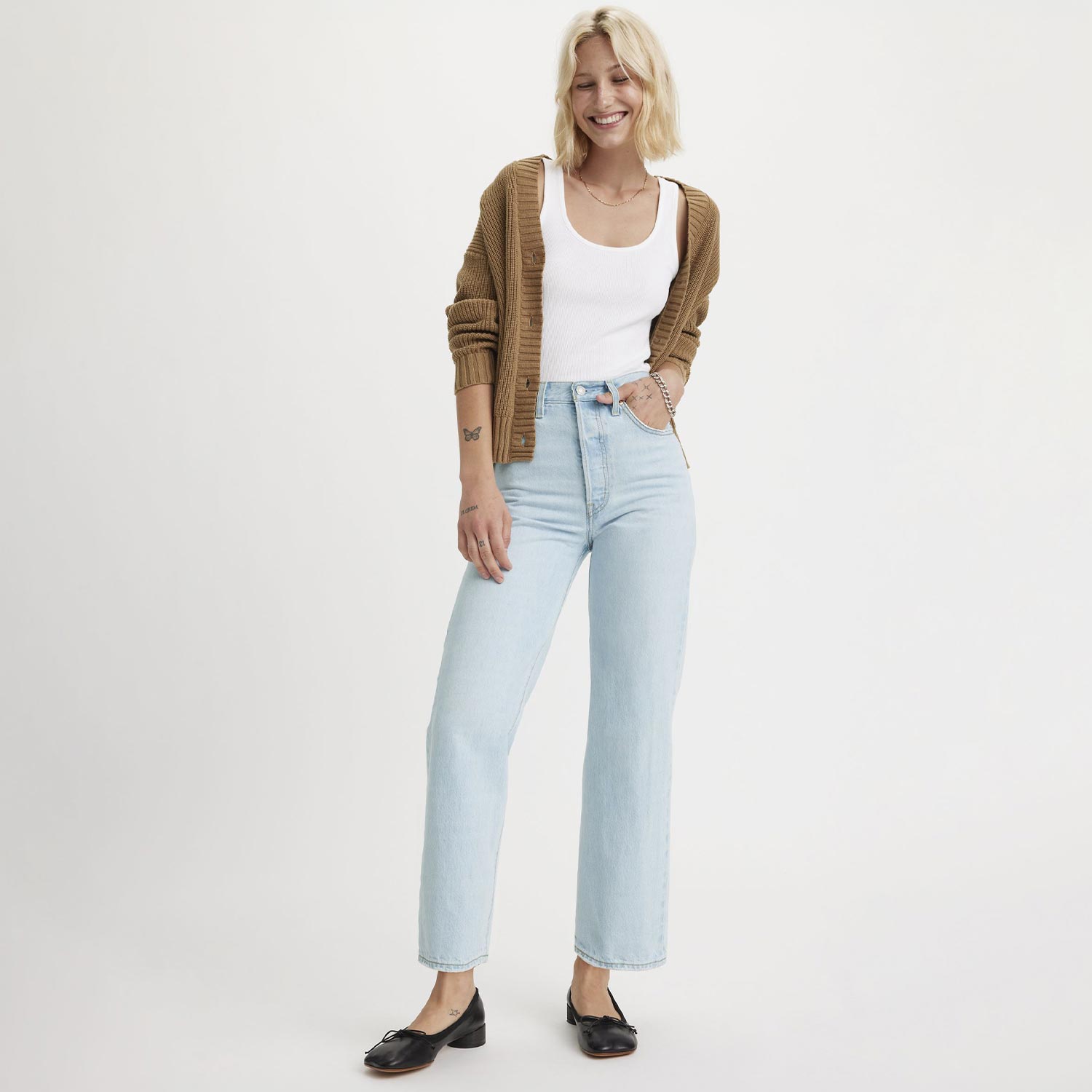Woman wearing light-wash straight-leg denim jeans with white vest and tan cardigan