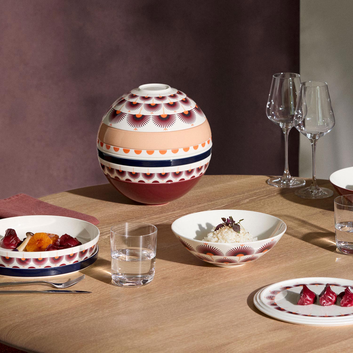 Dining table set with patterned dinnerware in red, white and navy, wine glasses and place settings with food
