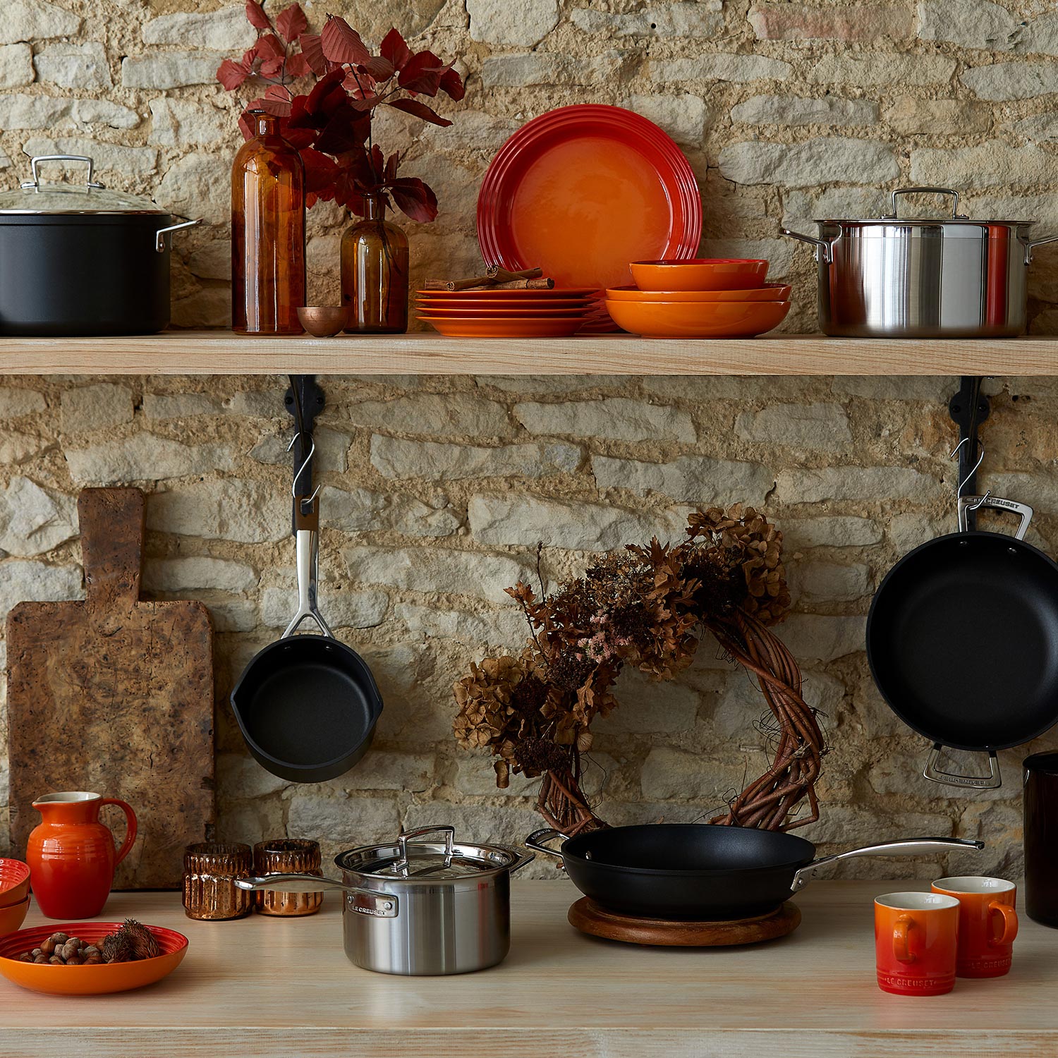 Kitchen display with orange and red cookware, pans, plates, and accessories against stone brick wall