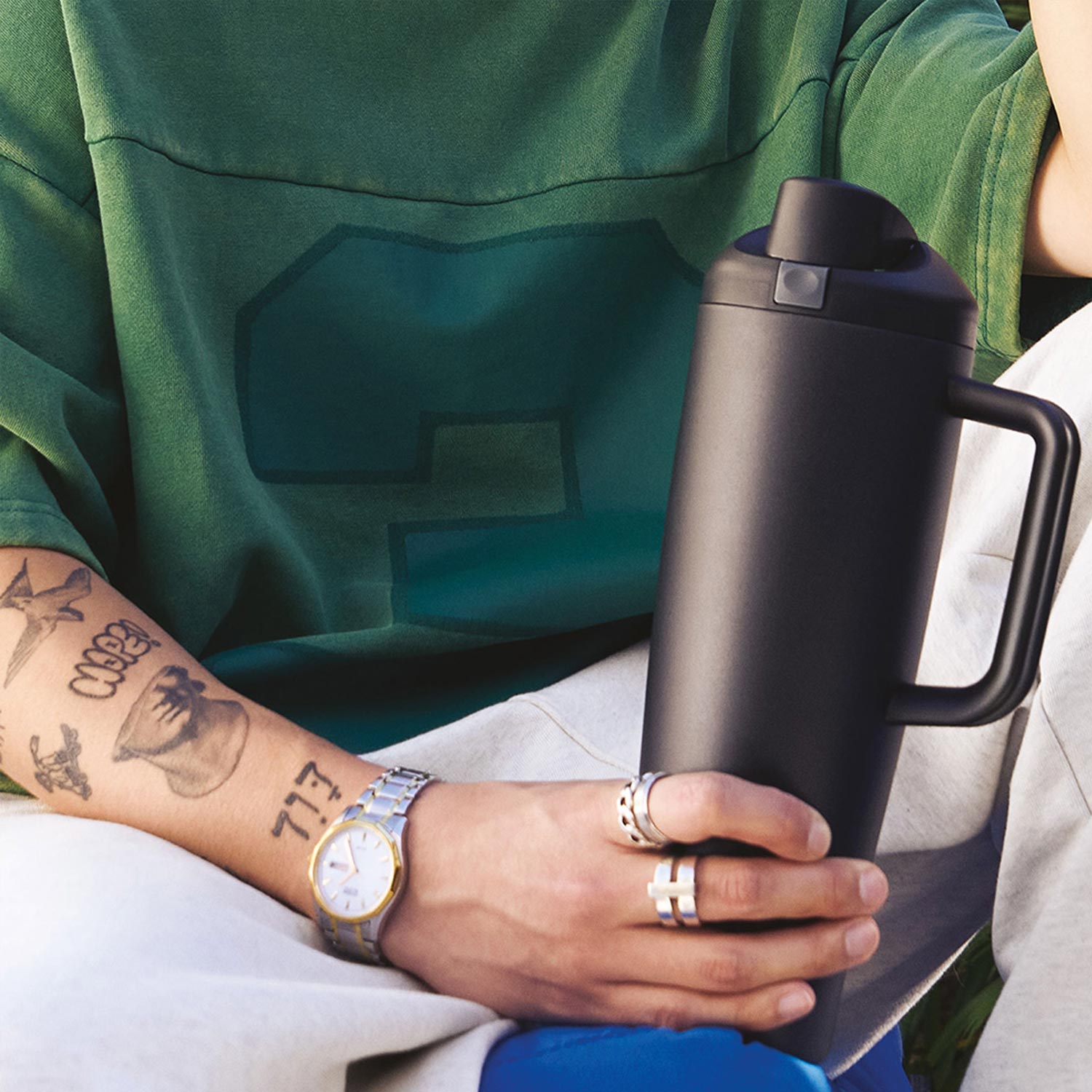 Person wearing green cardigan holding black Owala tumbler with white interior visible