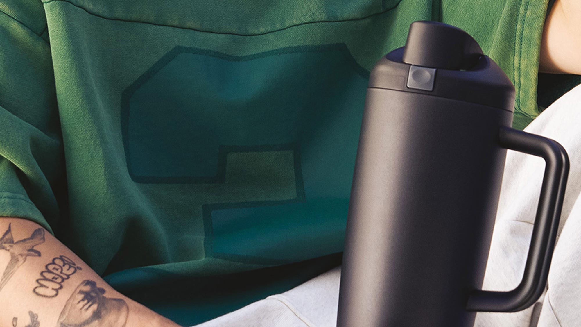 Person wearing green cardigan holding black Owala tumbler with white interior visible