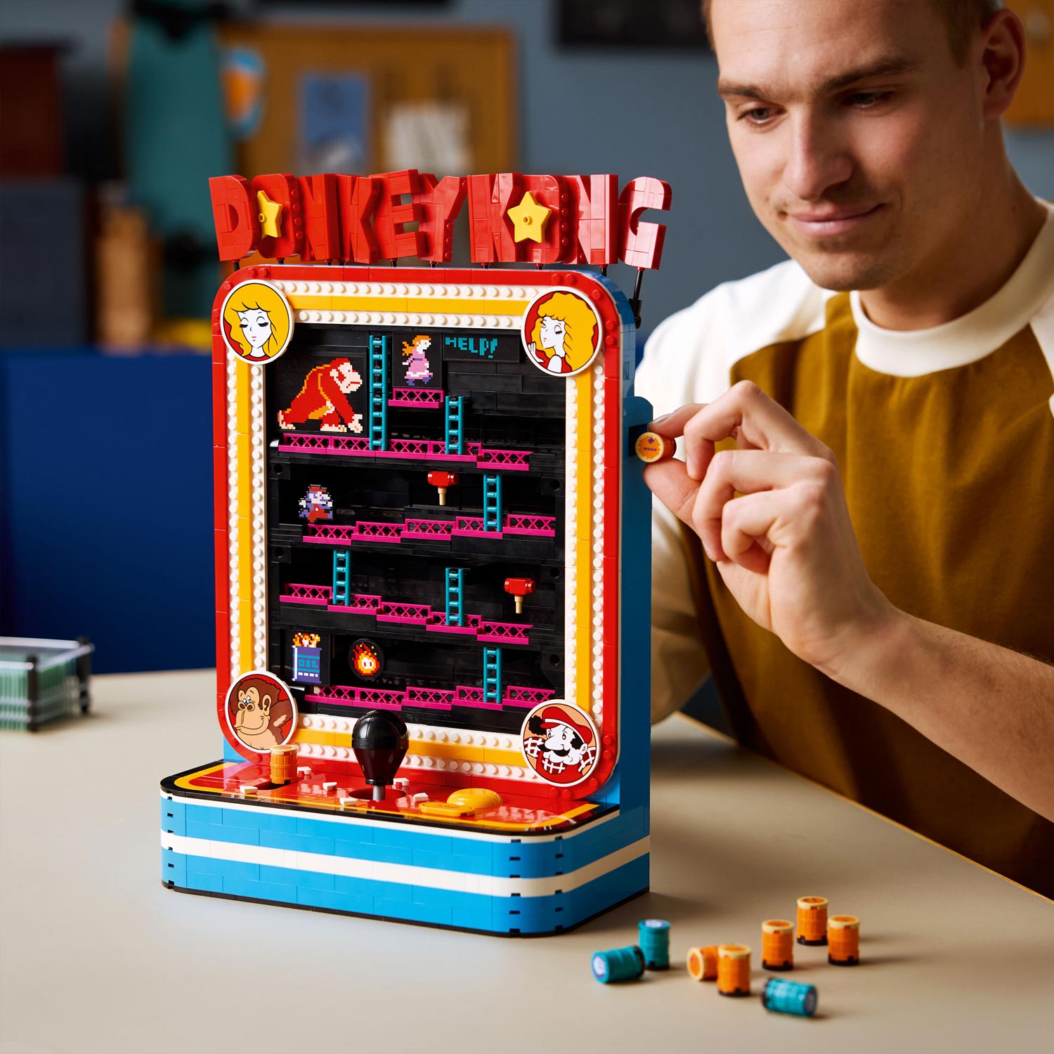 Man playing with LEGO Donkey Kong arcade game set featuring red marquee, pixel-art characters, and interactive joystick