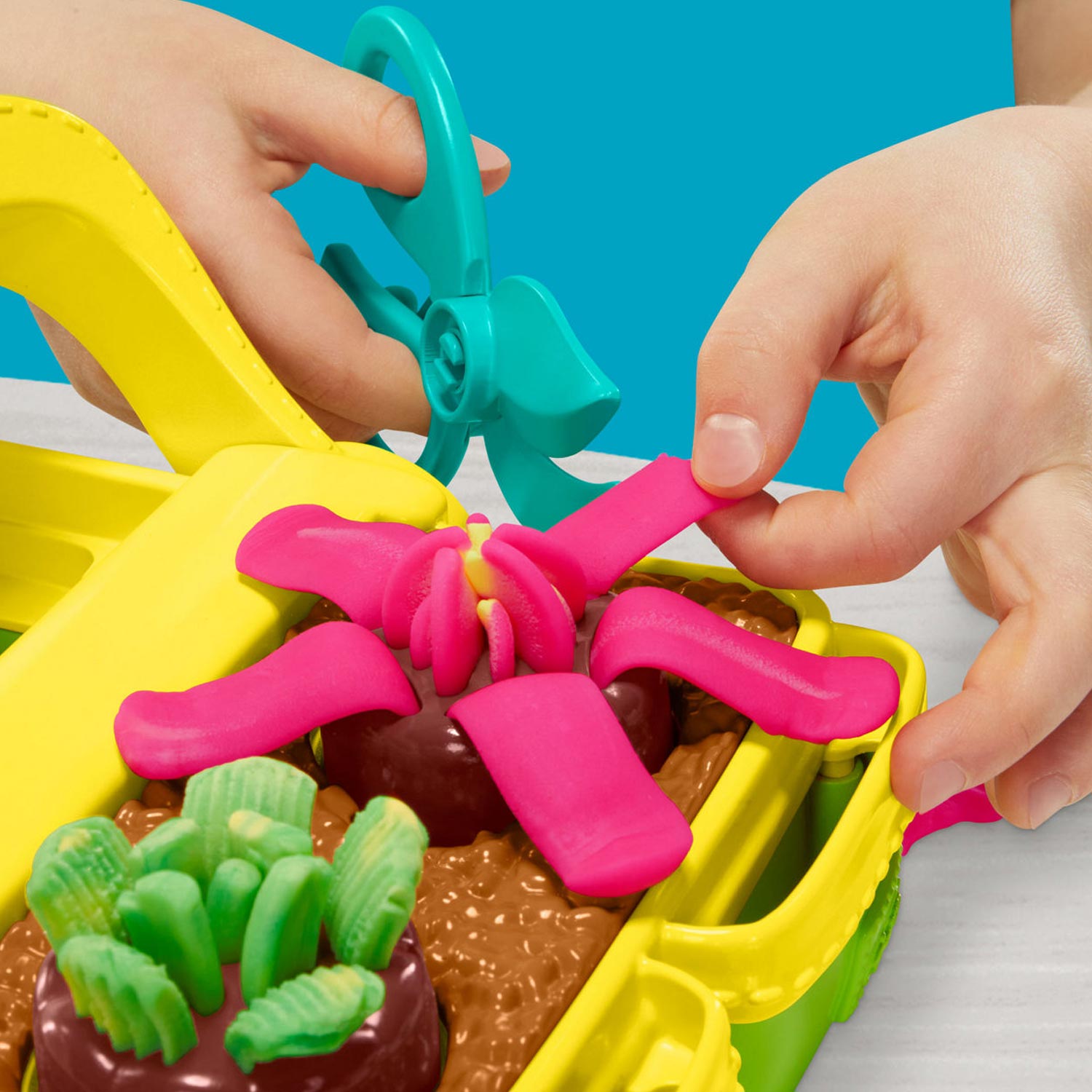 Child's hands manipulating brightly coloured Play-Doh compound in yellow, pink, green and brown with tools