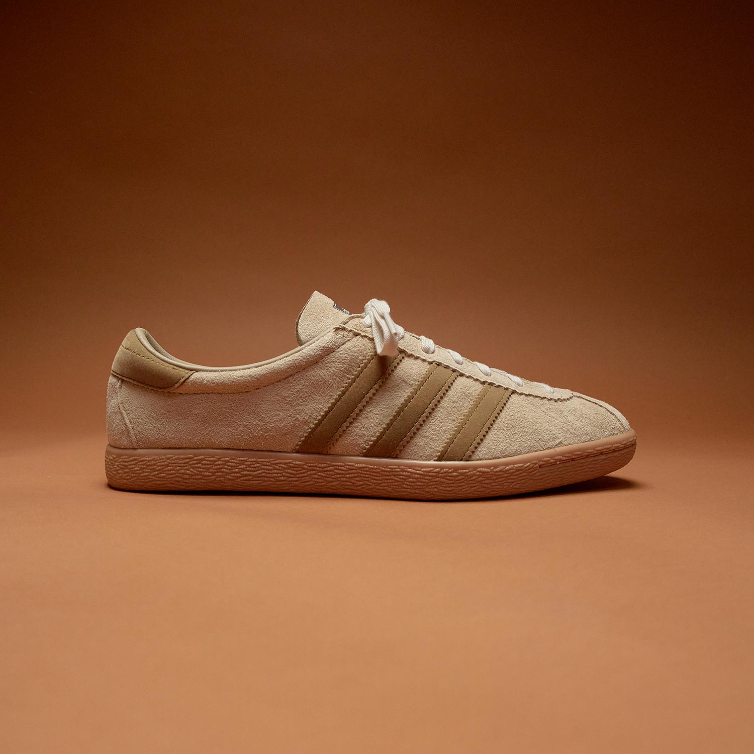 Cream suede lace-up trainers with contrast striped detail and gum sole against warm orange background