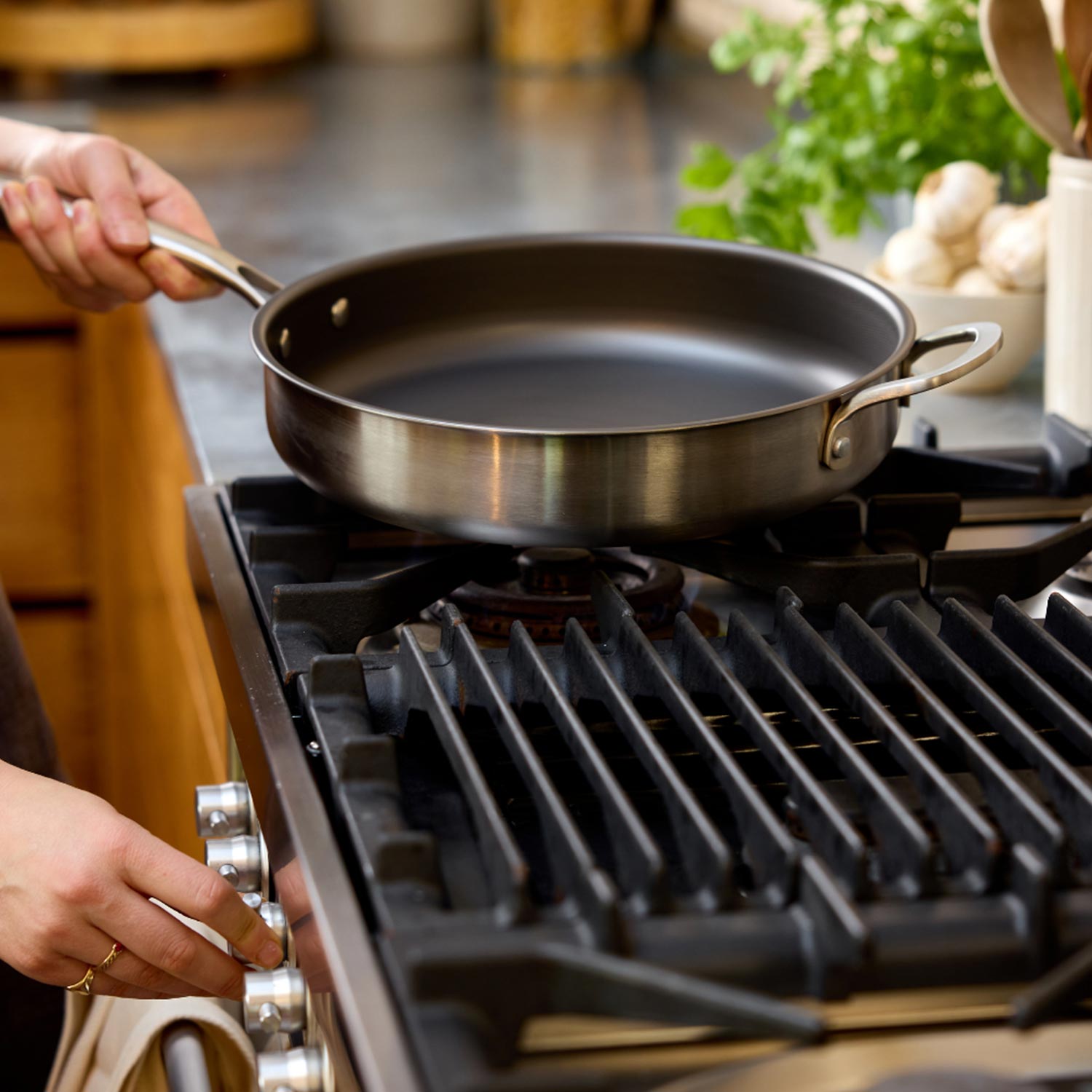 Non-stick frying pan on gas hob with fresh herbs and vegetables nearby