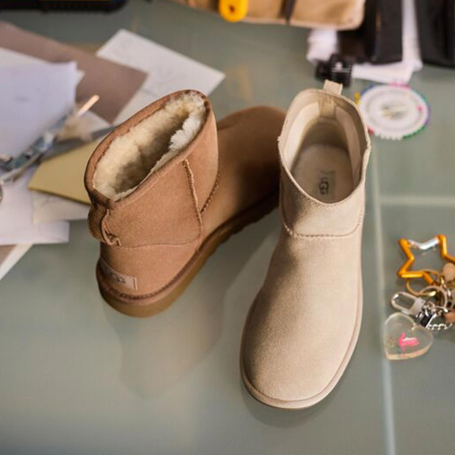 Two UGG boots in tan and cream with sheepskin lining displayed on grey surface