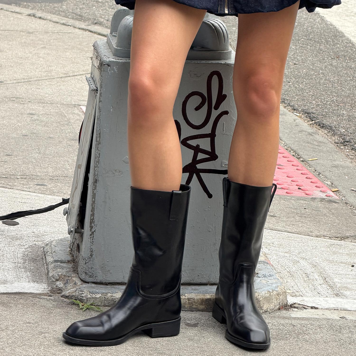 Person wearing black knee-high leather boots with chunky heel, standing outdoors