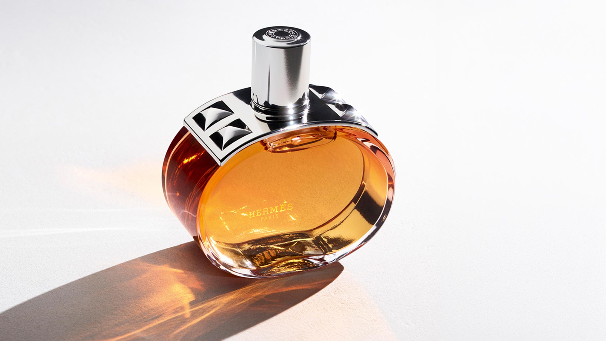 Hermès Barénia Pleine Fleur Eau de Parfum bottle with golden amber liquid and silver cap on neutral background