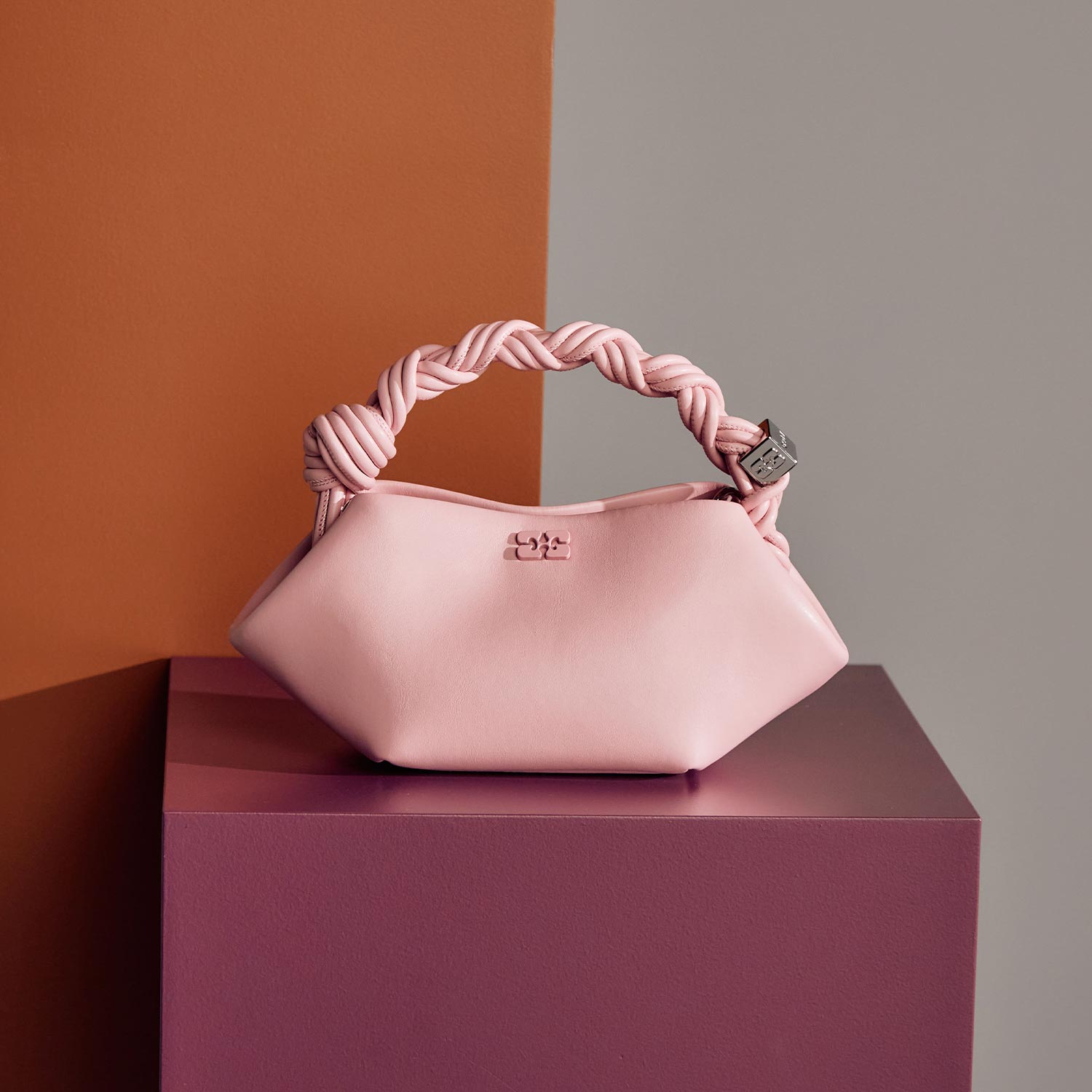 Light pink leather handbag with twisted rope handle and metal logo detail on purple platform