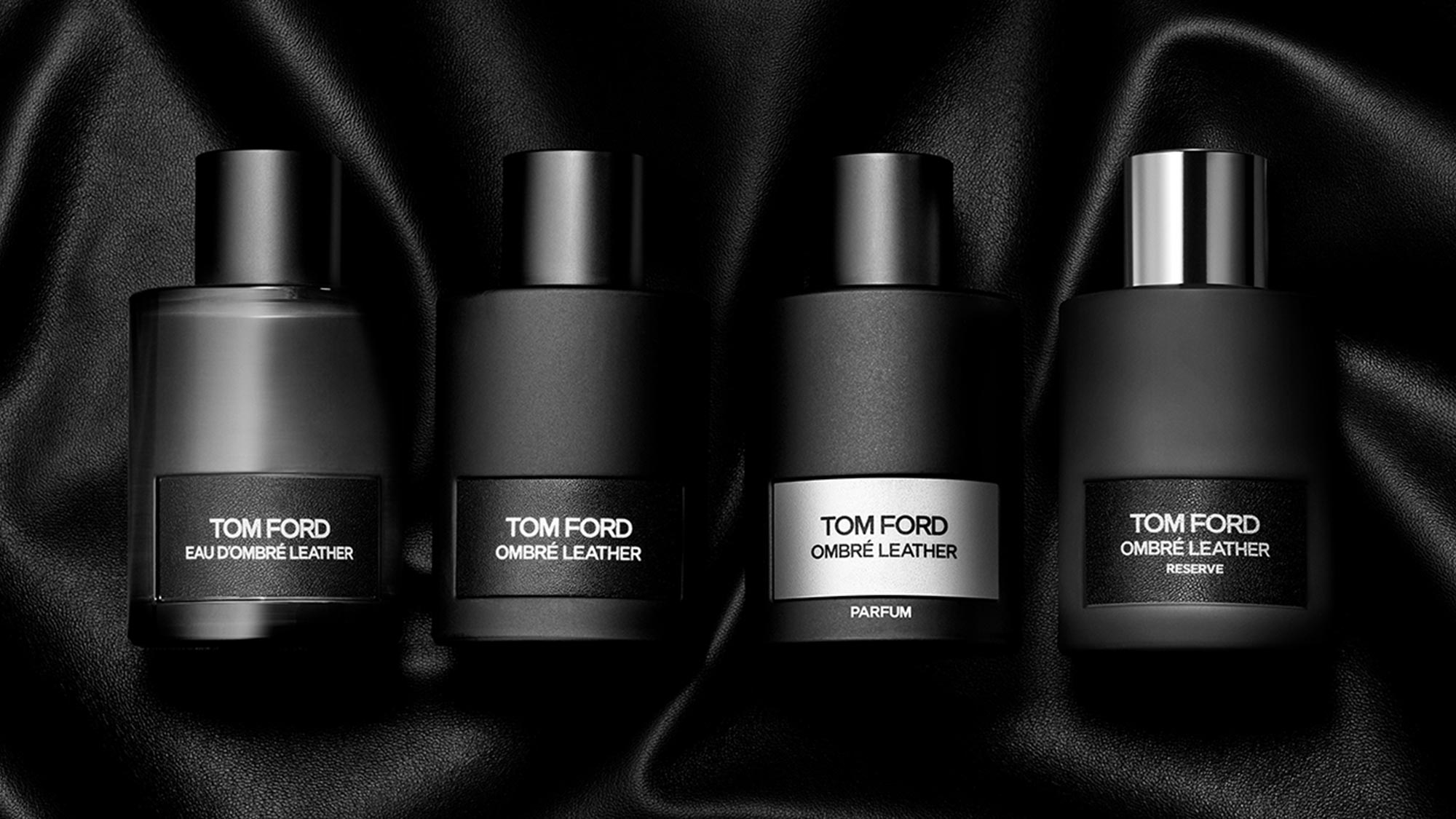 Four Tom Ford Ombré Leather fragrance bottles with silver caps against black silk fabric backdrop