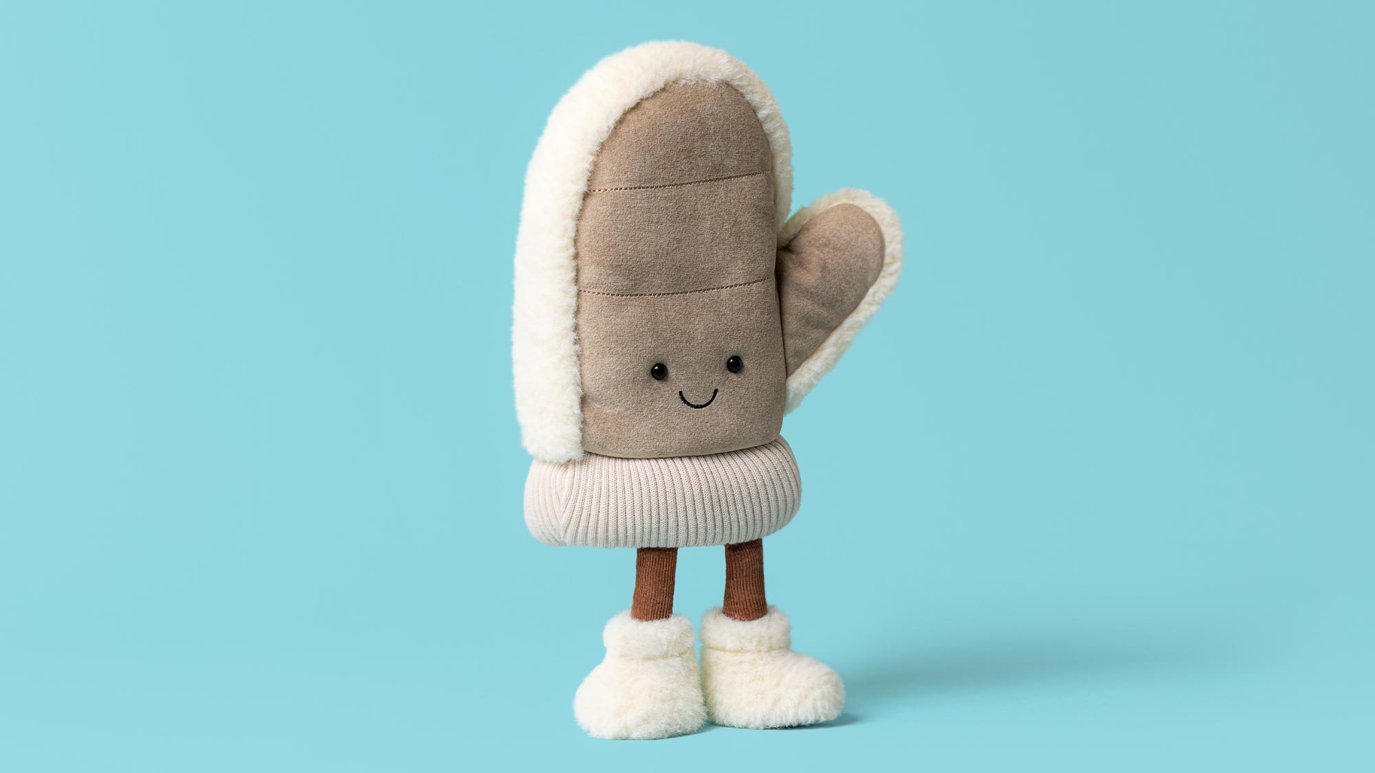 Plush toy mitten character with smiling face, beige fabric with cream fleece trim and brown legs against blue background