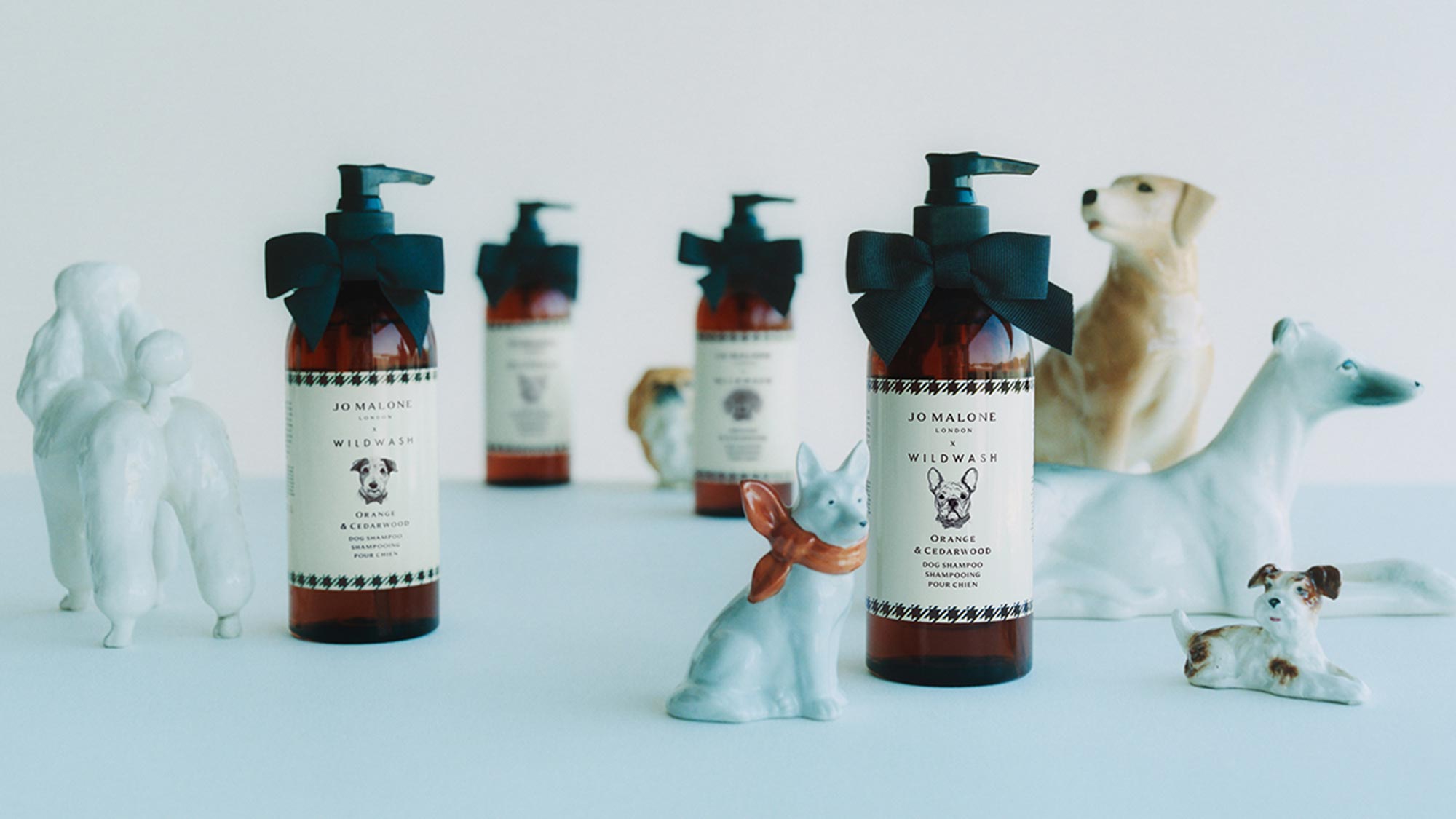 Jo Malone London Wildwash dog shampoo bottles with teal bows surrounded by white ceramic dog figurines