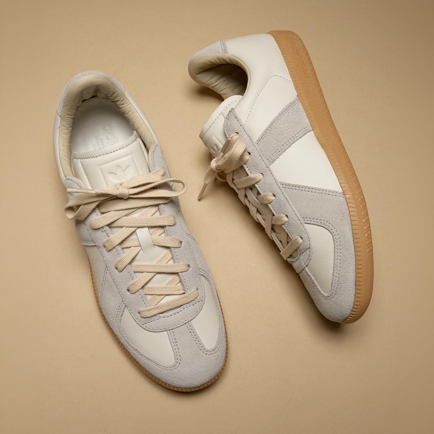 Pair of cream and beige suede trainers with lace-up fastening and gum sole on neutral background