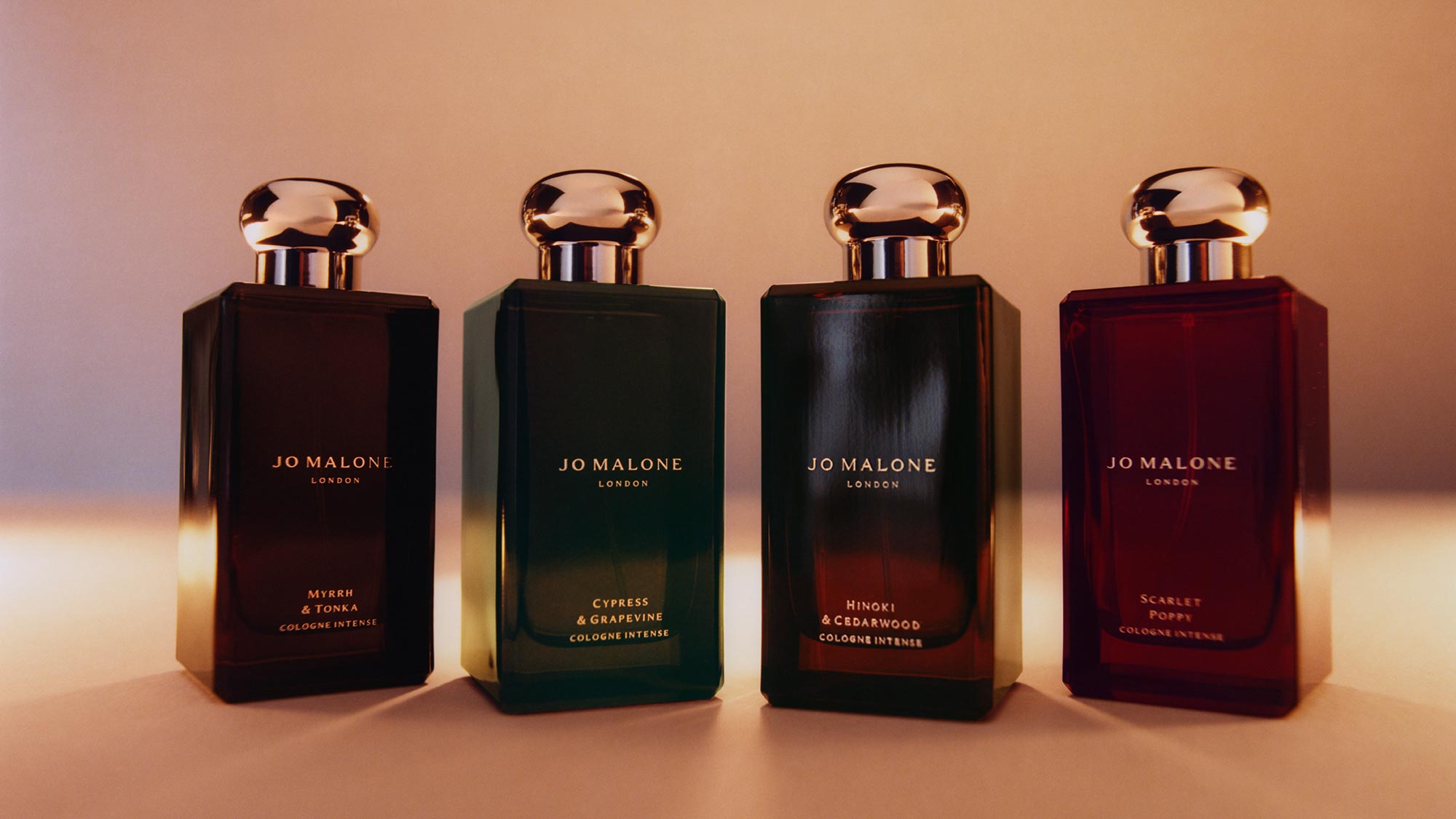 Four Jo Malone London Cologne Intense bottles with gold caps in dark glass bottles labelled Myrrh & Tonka, Cypress & Grapevine, Hinoki & Cedarwood, and Scarlet Poppy