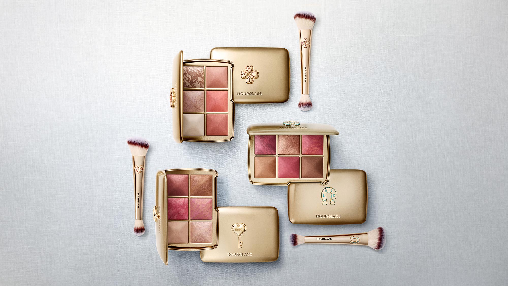 Hourglass Ambient Lighting Edit collection with eyeshadow palettes, blush compacts, makeup brushes and highlighter in gold packaging with pink and bronze tones
