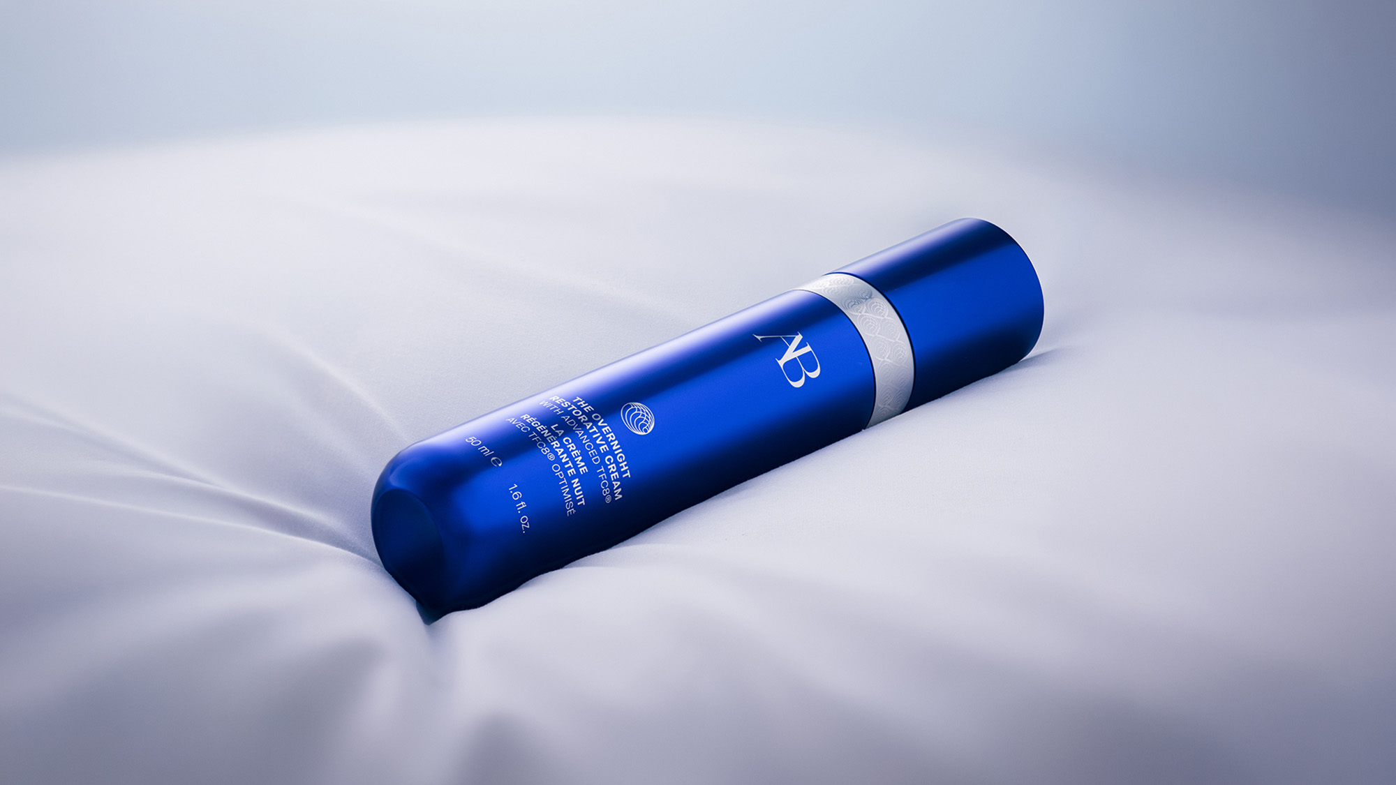 Blue cylindrical bottle of Augustinus Bader Overnight Restorative Cream with white band detail on light background.
